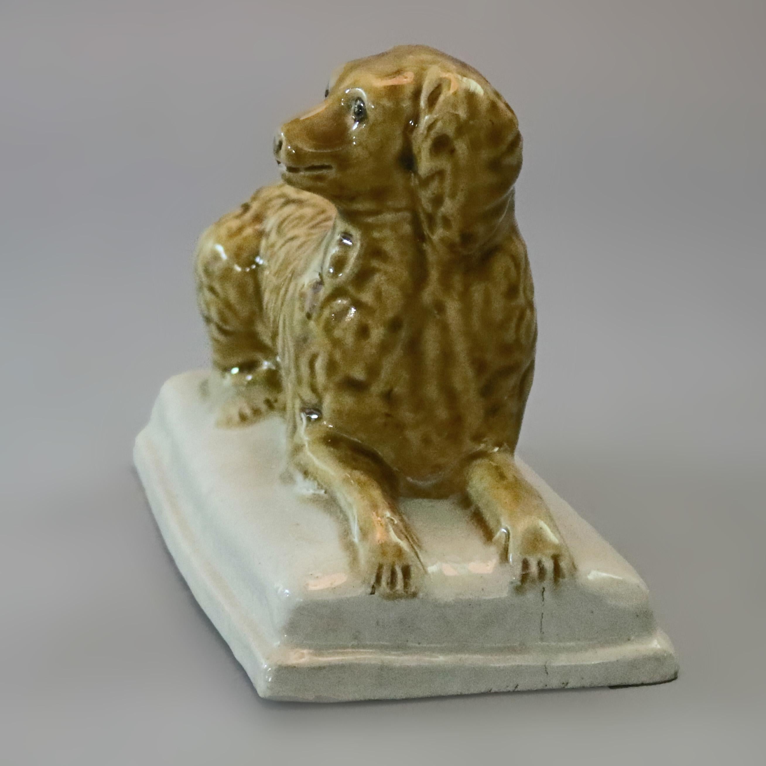 An antique glazed stoneware (possibly yellow ware) canine sculpture depicts recumbent dog on base, reminiscent of the Irish Water Spaniel and later Staffordshire, circa 1850

Measures - 5.5