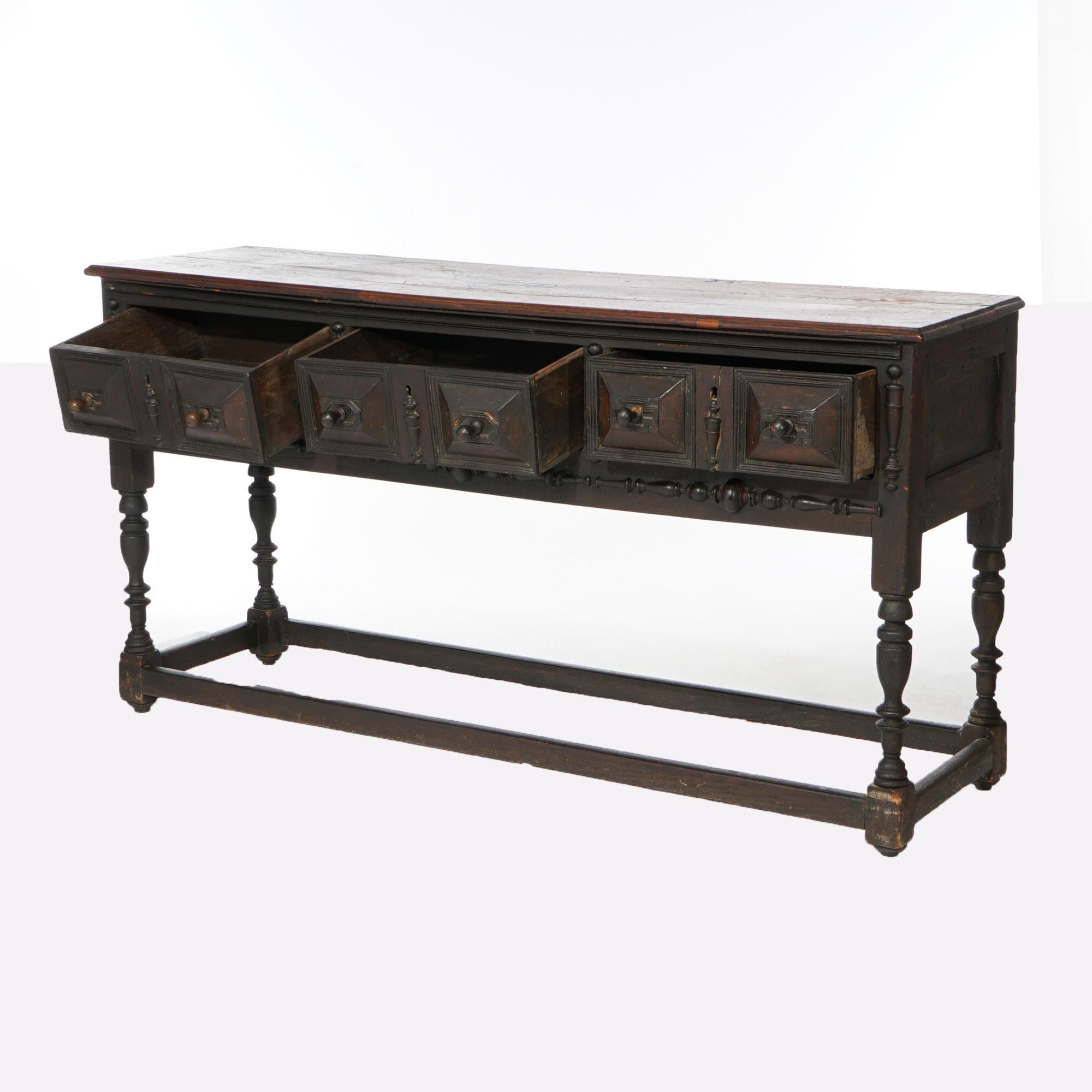 An antique Jacobean sideboard offers English oak construction with three drawers with carved pyramidal elements, raised balustrade legs and stretcher base, 18th century

Measures- 32.5''H x 62.25''W x 19.5''D