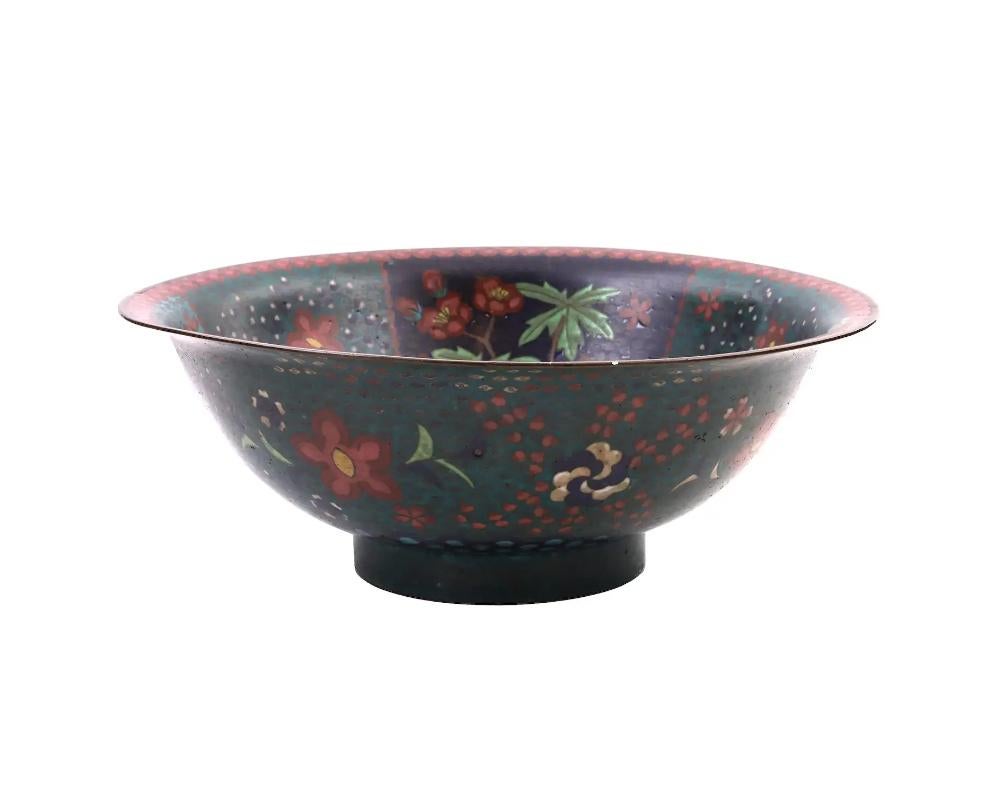 An antique Japanese, Meiji period, footed enamel over copper bowl. The interior of the bowl is adorned with polychrome enamel panels depicting blossoming flowers surrounded by a swirl motif, and a round shaped medallion depicting a scene with