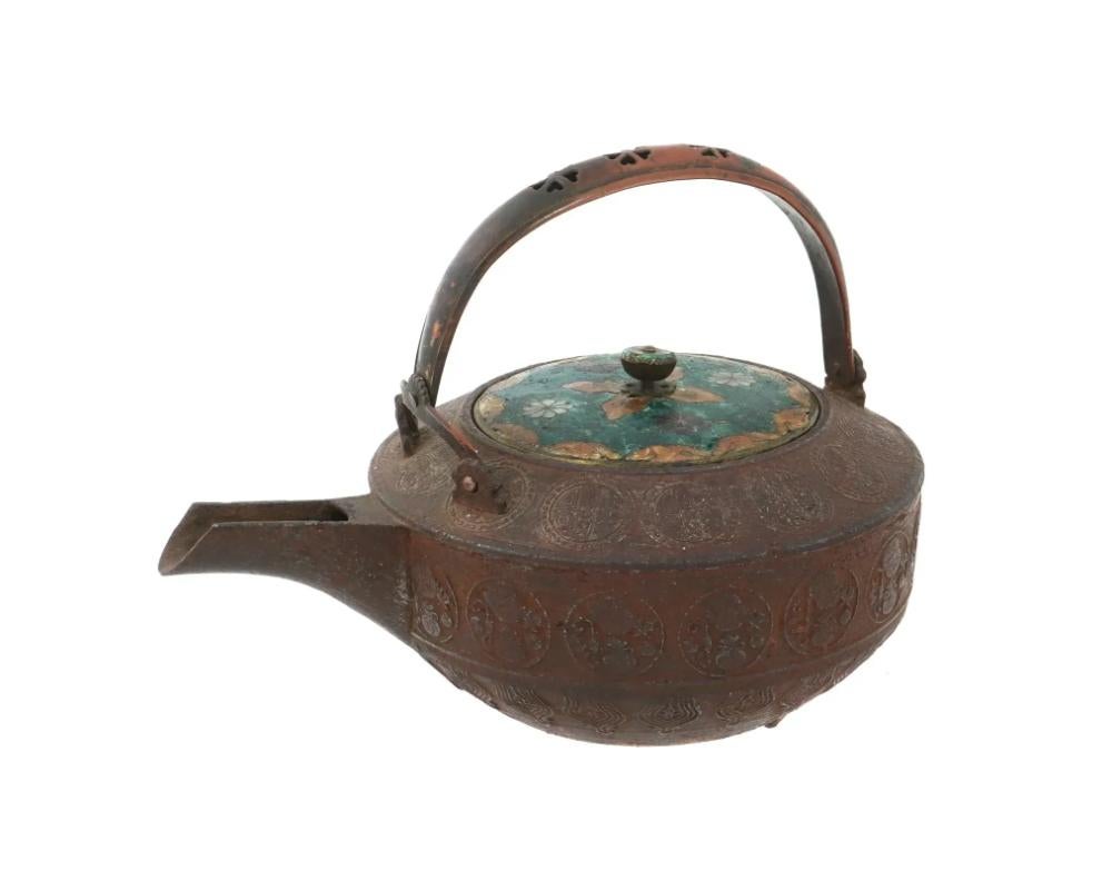 An antique Japanese Meiji Era lidded copper tea pot. Circa: late 18th century to early 19th century. The body of the ware is adorned with impressed medallions. The lid of the pot is adorned with polychrome floral and foliage ornaments made in the