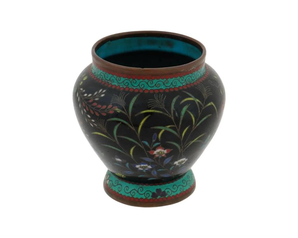 An antique Japanese vase from the early Meiji period, decorated with enamel using the cloisonne technique. The wide vase with a slightly narrowed neck. The surface is decorated with a large number of flowers and herbs of different colors on black