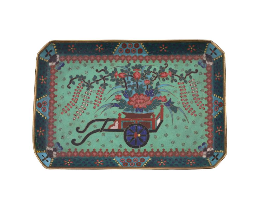 An antique Japanese, Meiji period, enamel tray. The octagonal shaped tray is enameled with a polychrome image of a wagon with blossoming Wisteria and other flowers surrounded by a swirl motif on the green ground made in the Cloisonne technique. The