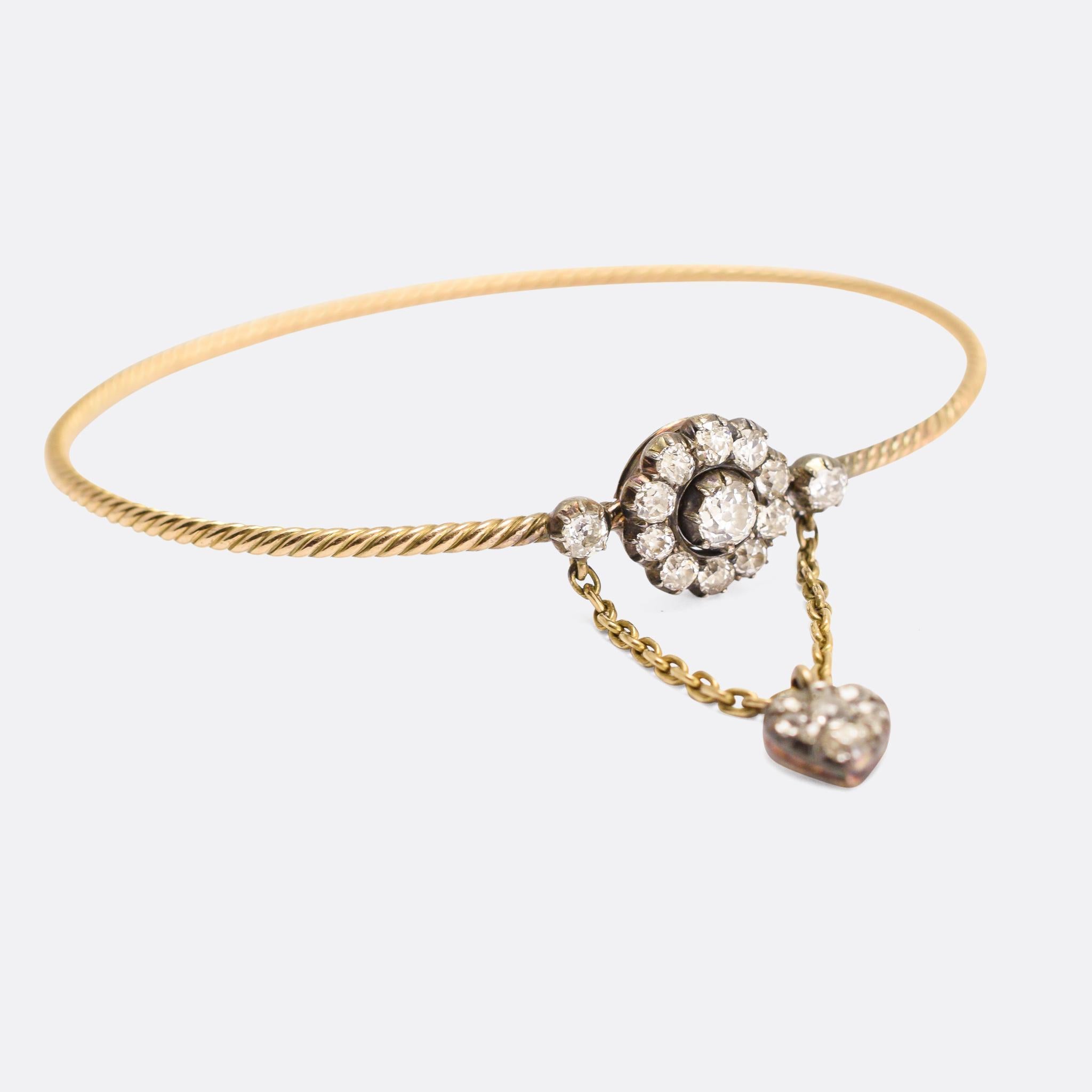 A stunning antique bangle dating from the mid-19th Century, circa 1840. The head is modelled as a flower, set with bright old mine cut diamonds, with a diamond-set heart drop dangling freely beneath. The gold band has been crafted with a twist motif