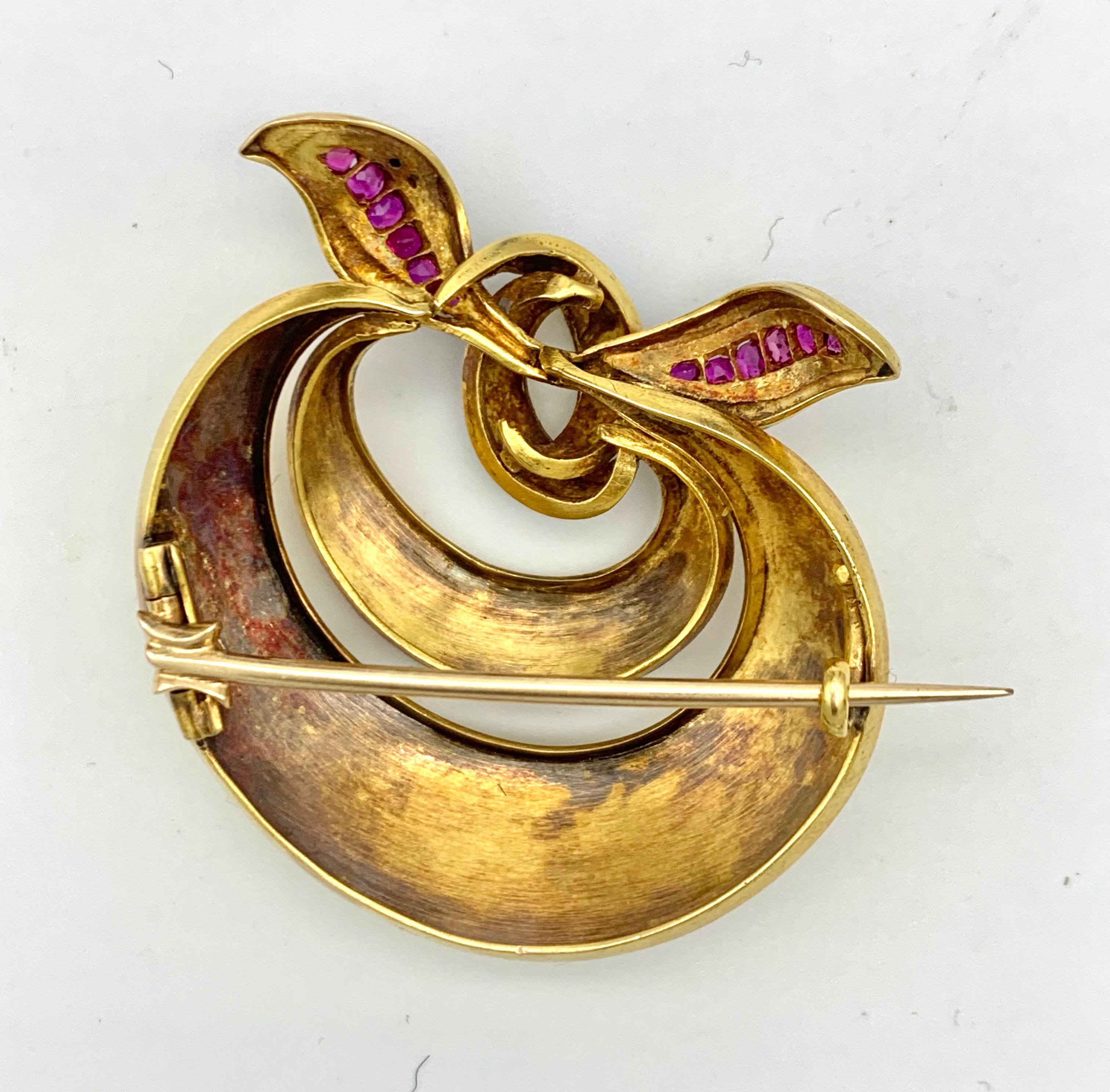 This early Victorian brooch was hand crafted from 15 karat gold and finely engraved with foliage framed by ornamental borders. The two gold hoops are held together by a pale blue enamelled gold ribbon set with natural rubies.