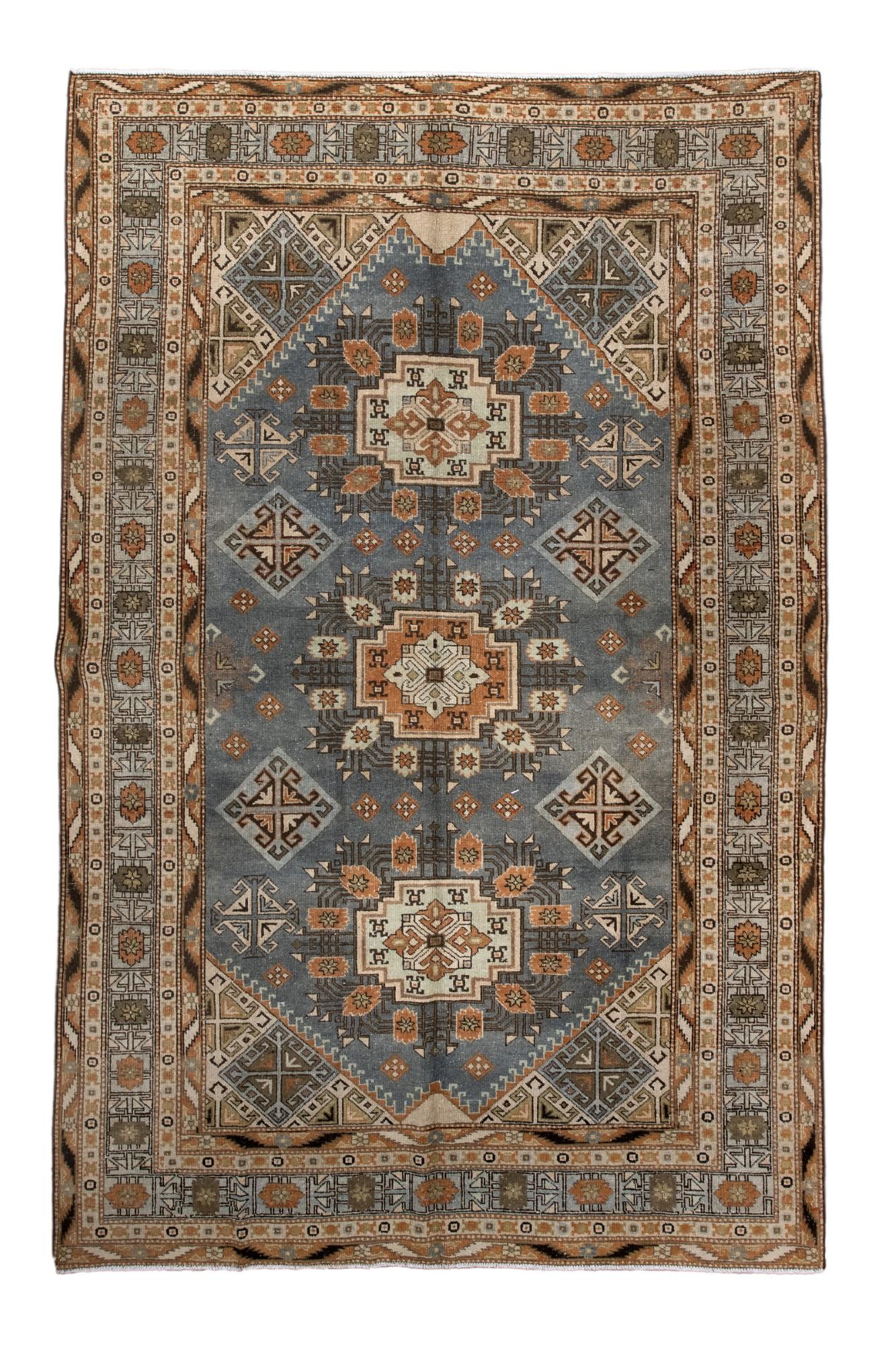 Ce tapis Khotan ancien présente un arrangement classique de médaillons géométriques sur un champ bleu doux, accentué par des fleurs stylisées et des motifs angulaires. De multiples bordures traditionnelles du Khotan encadrent le dessin, lui