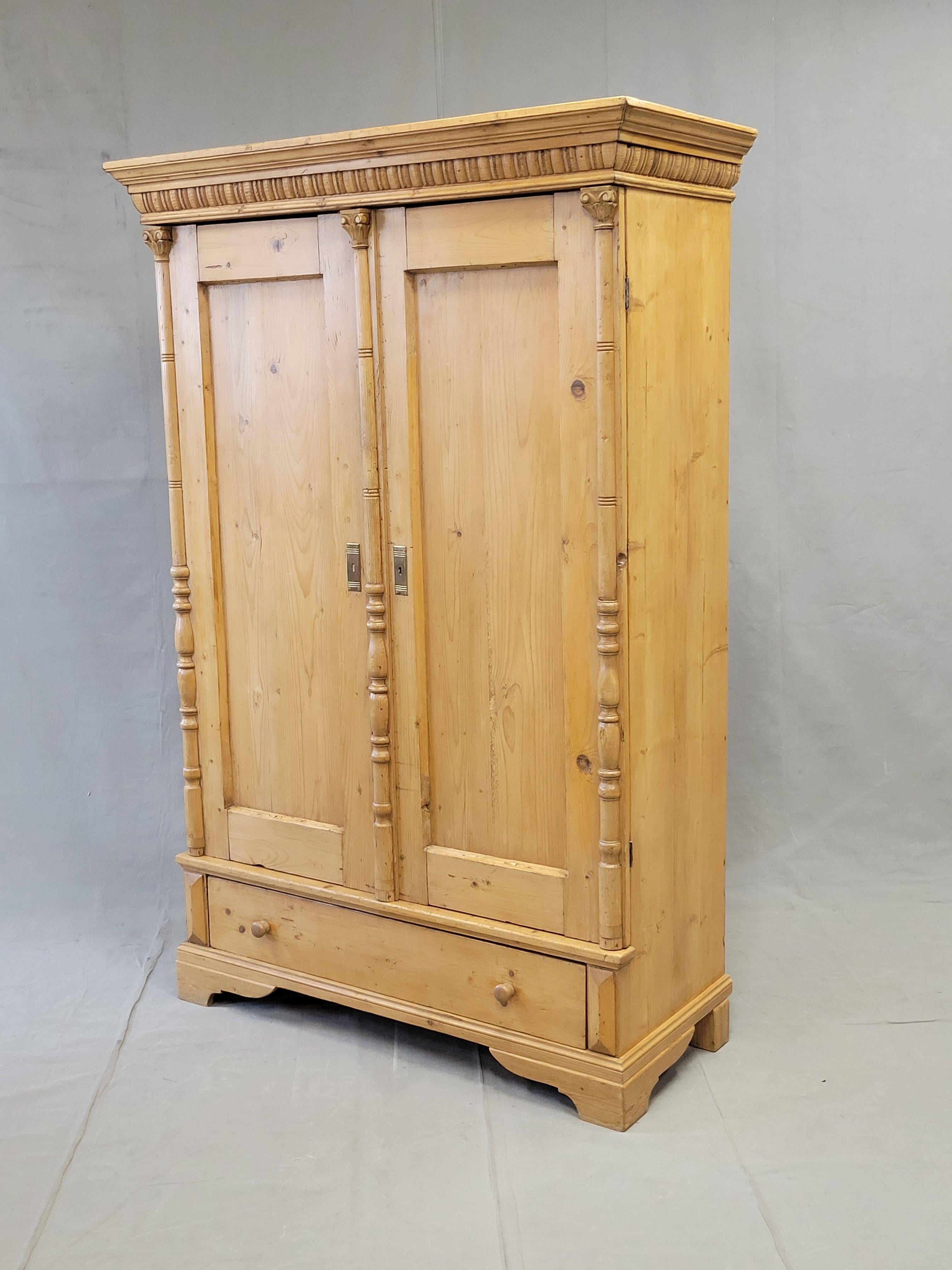 A beautiful and functional antique circa 1900 pine Eastern European wardrobe with three interior shelves and a bottom drawer. The Corinthian turned pilasters flanking the doors and center astegral give the armoire a decorative accent. The crown is