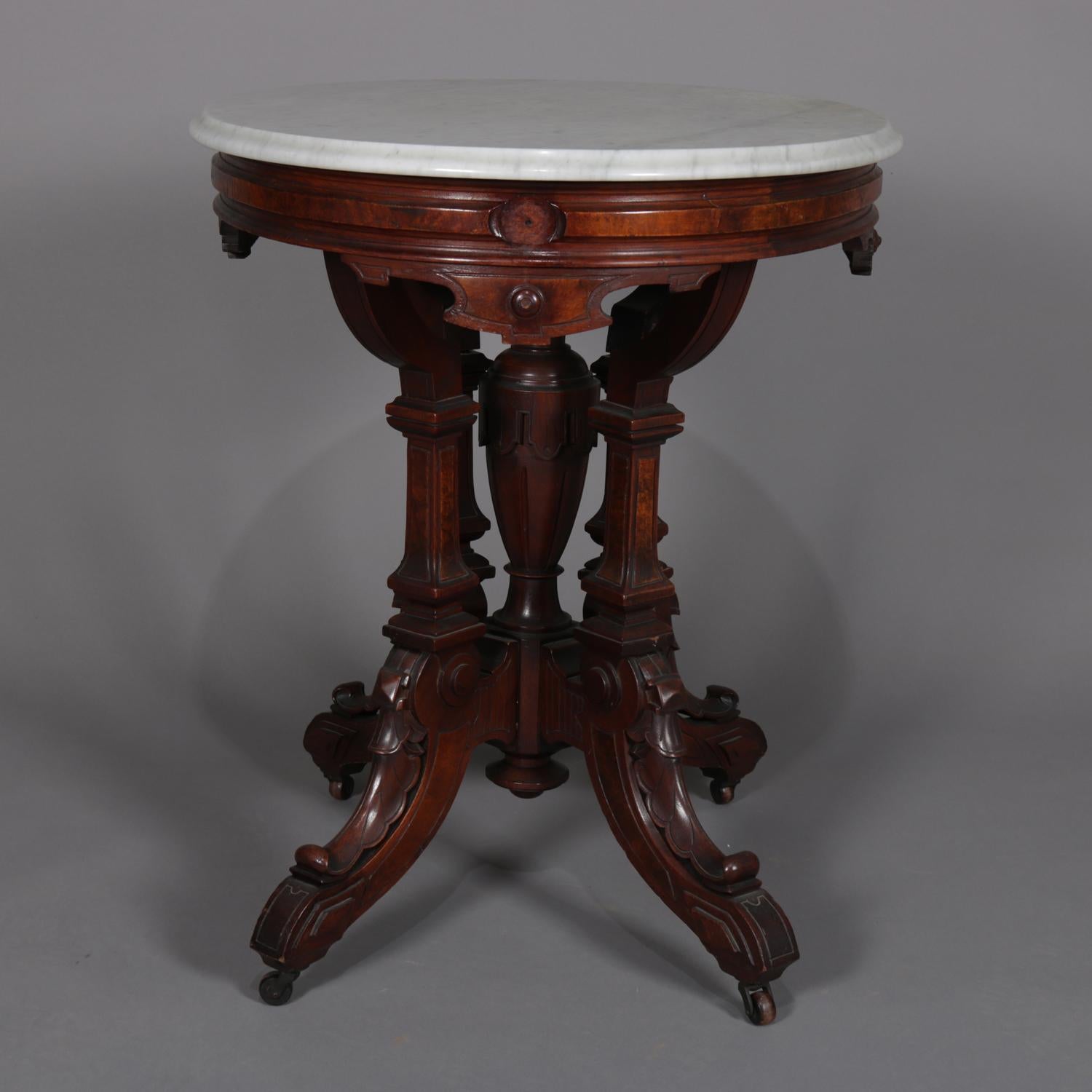 Antique Victorian Eastlake centre table features oval form with bevelled marble-top surmounting carved walnut base having carved apron with burl inset over central urn form pedestal and surround of four foliate carved legs on casters, circa