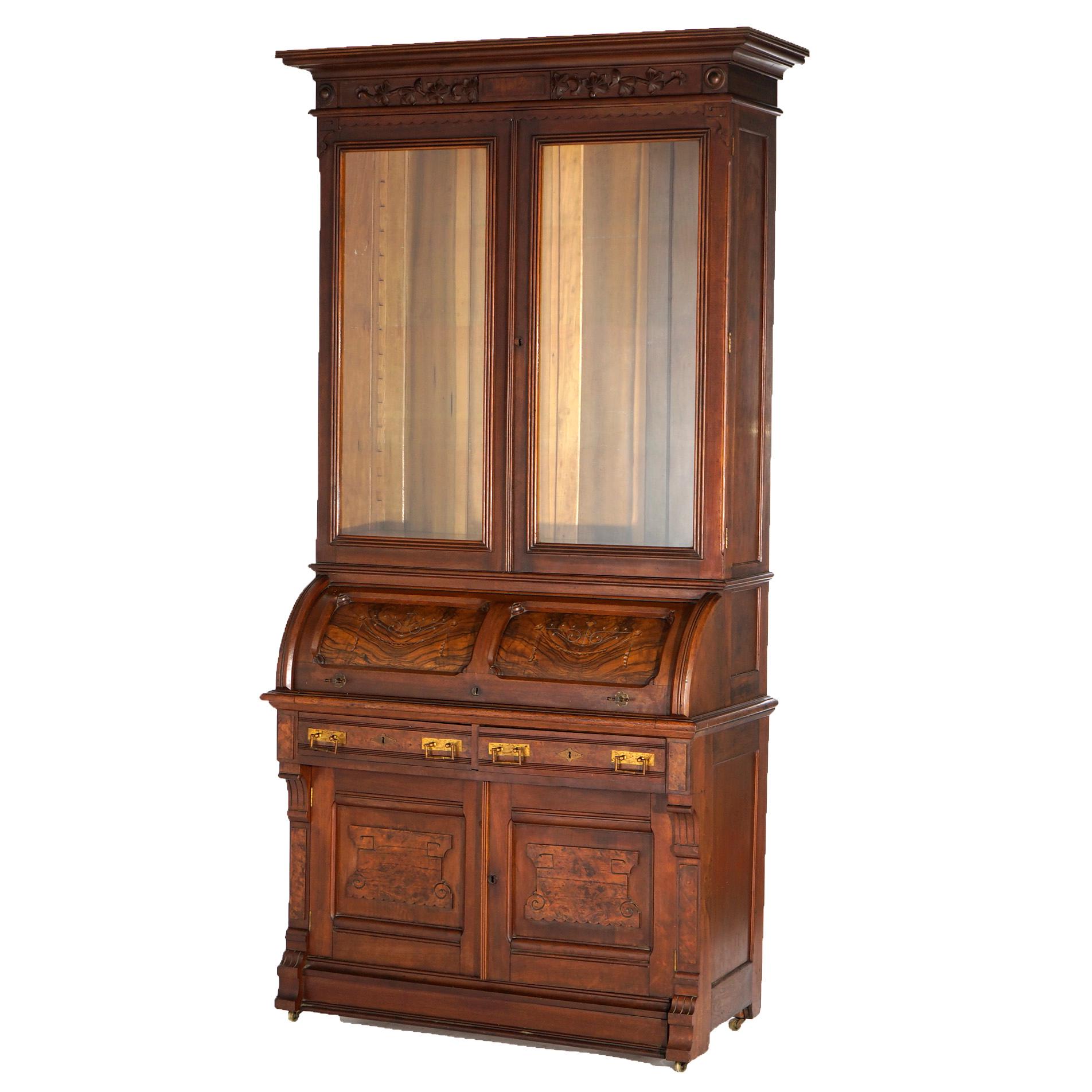 An antique Eastlake cylinder desk offers paneled walnut and burl construction with upper double glass door bookcase over barrel roll desk opening to writing surface and storage compartments, lower having double drawers over double door cabinet,