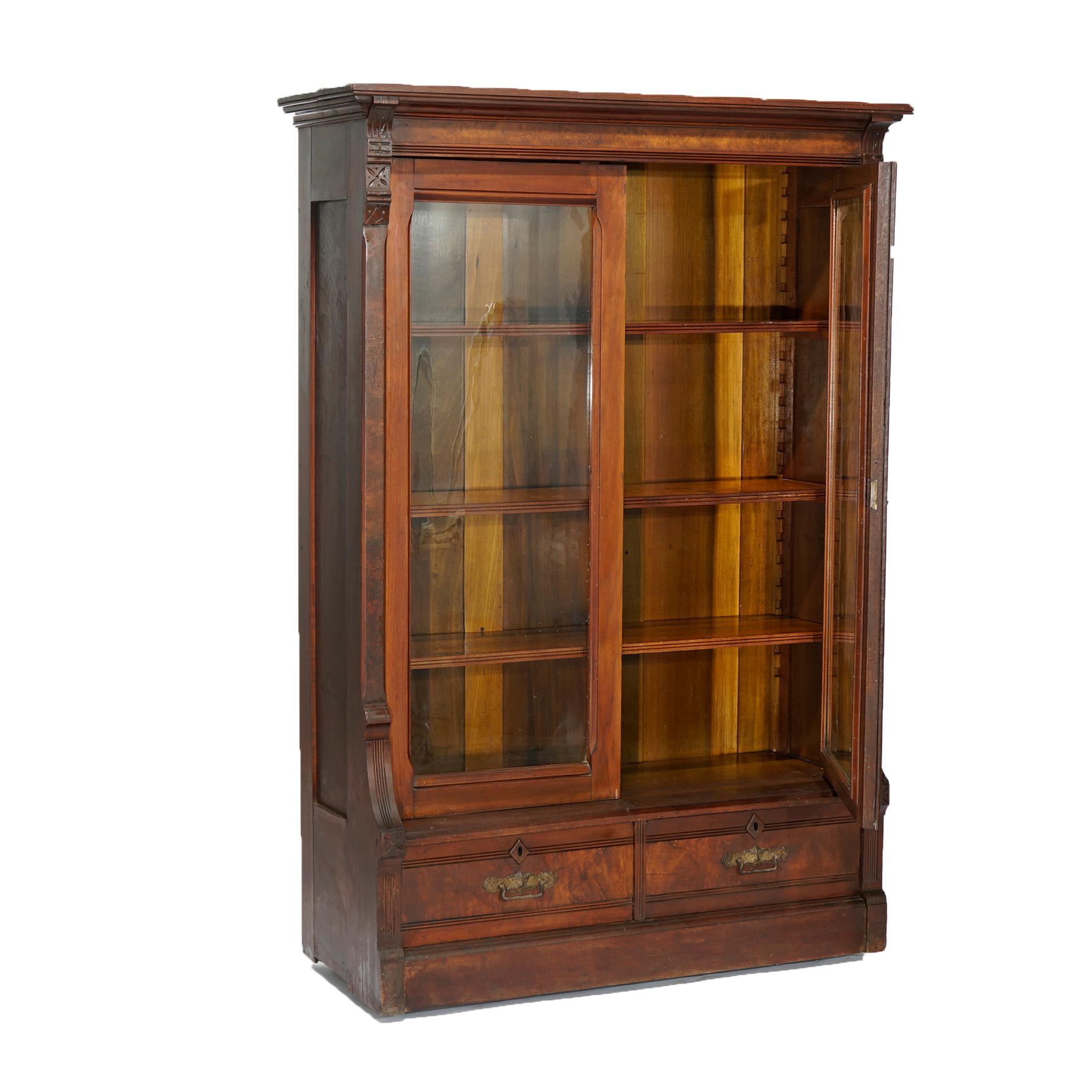 An antique Eastlake enclosed bookcase offers walnut and burl construction with double glass doors opening to adjustable shelf interior over base with two drawers, incised stylized flowers throughout, c1890.

Measures- 61.75''H x 42''W x 16.5''D.