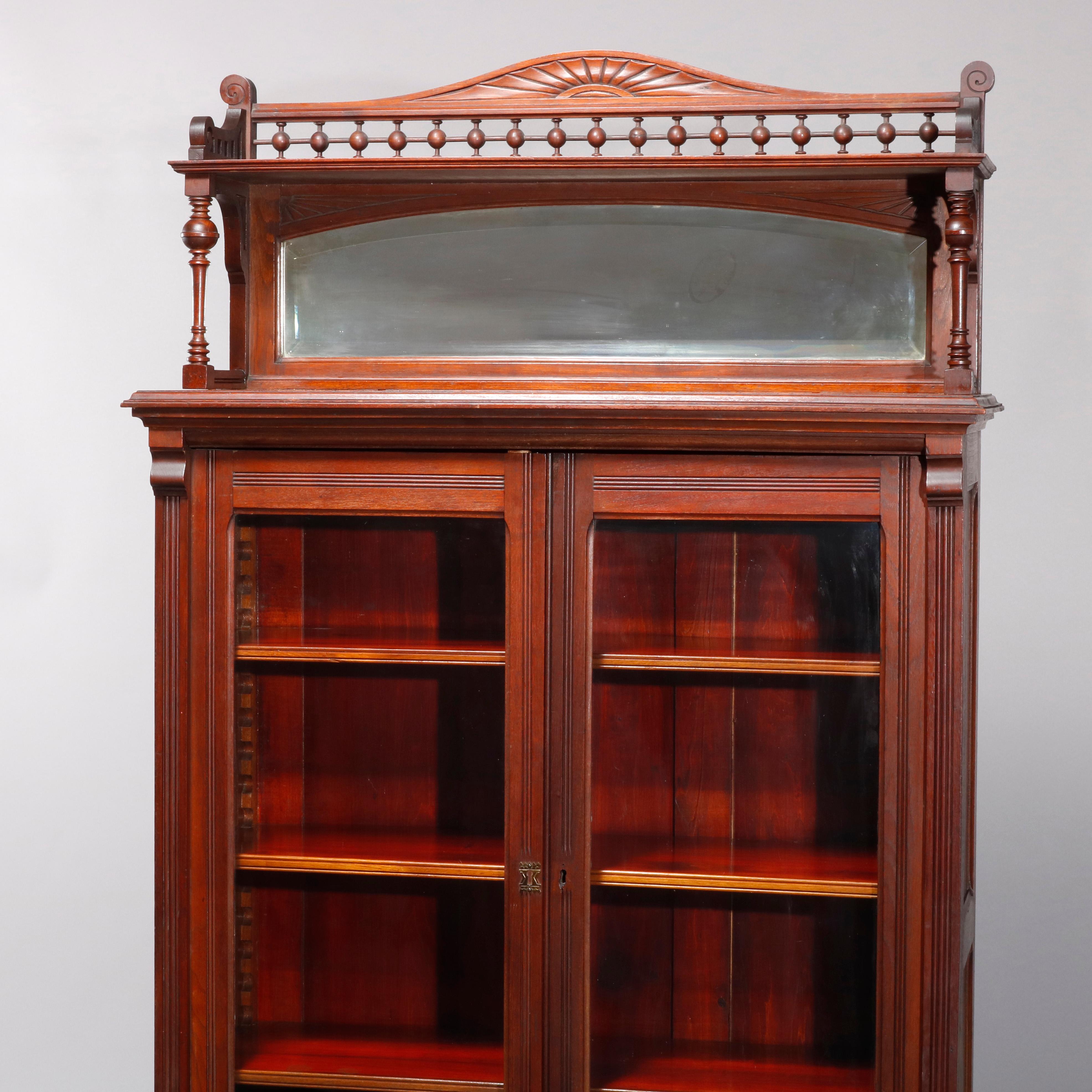 An antique Eastlake bookcase offers walnut construction with mirrored backsplash having shaped crest with stick and ball rais surmounting double glass door case opening to shelved interior, seated on base with two drawers, circa 1890

Measures: