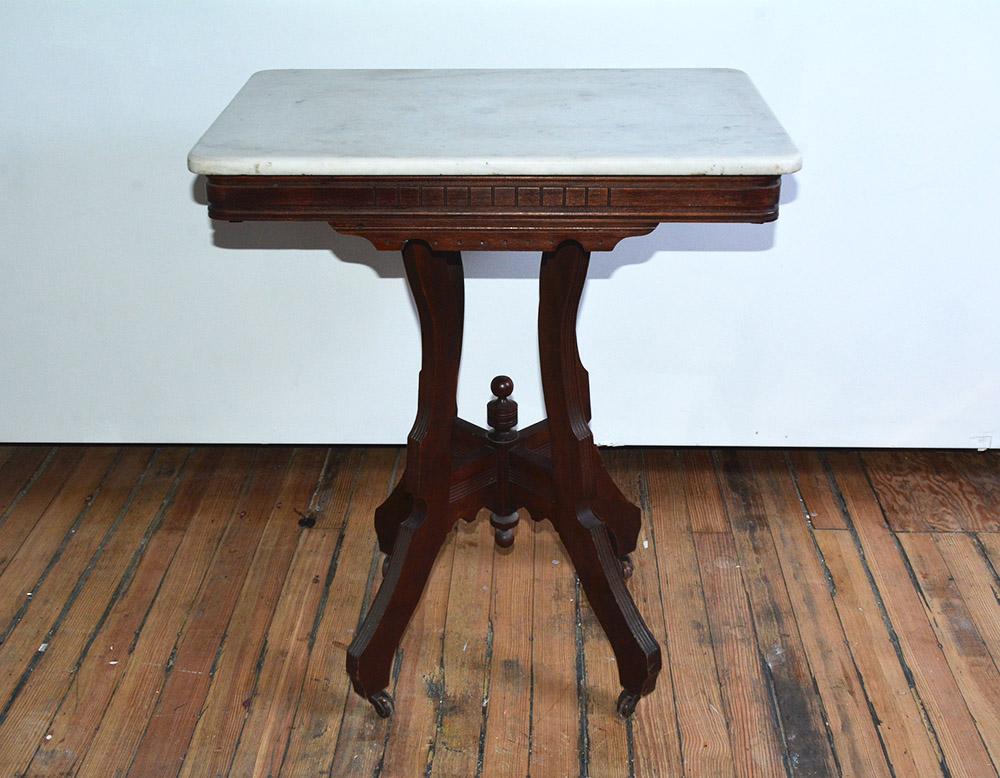 Ancienne table centrale victorienne de style Eastlake, avec plateau rectangulaire en marbre surmontant une base et un tablier en bois sculpté, sur un piédestal central tourné et un entourage de quatre pieds à roulettes, vers 1870. Peut être utilisée