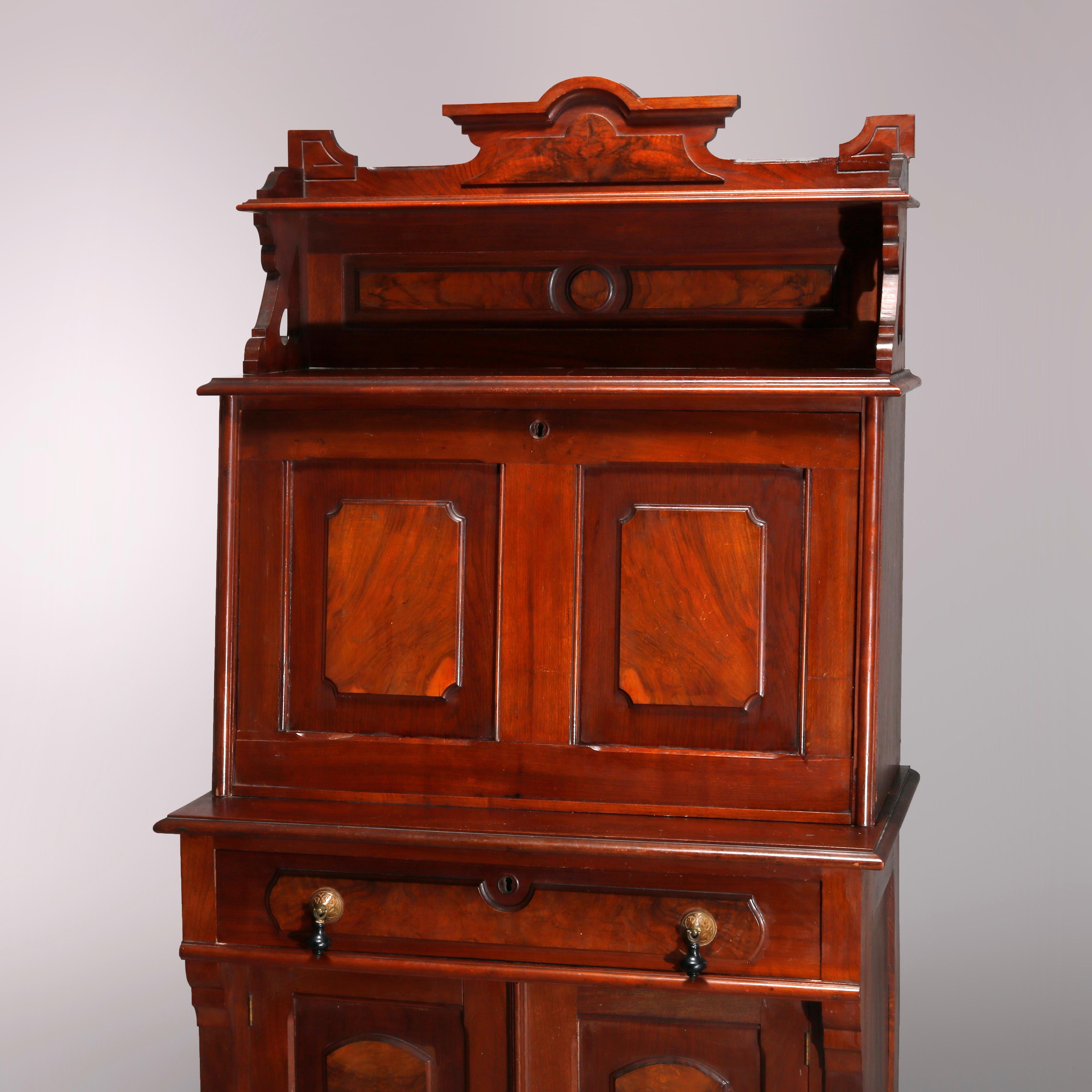 An antique Eastlake secretary offers paneled walnut construction with upper having shaped crest surmounting shelf and slant front opening to writing desk and storage compartments and pigeon holes, lower with single long drawer over double door