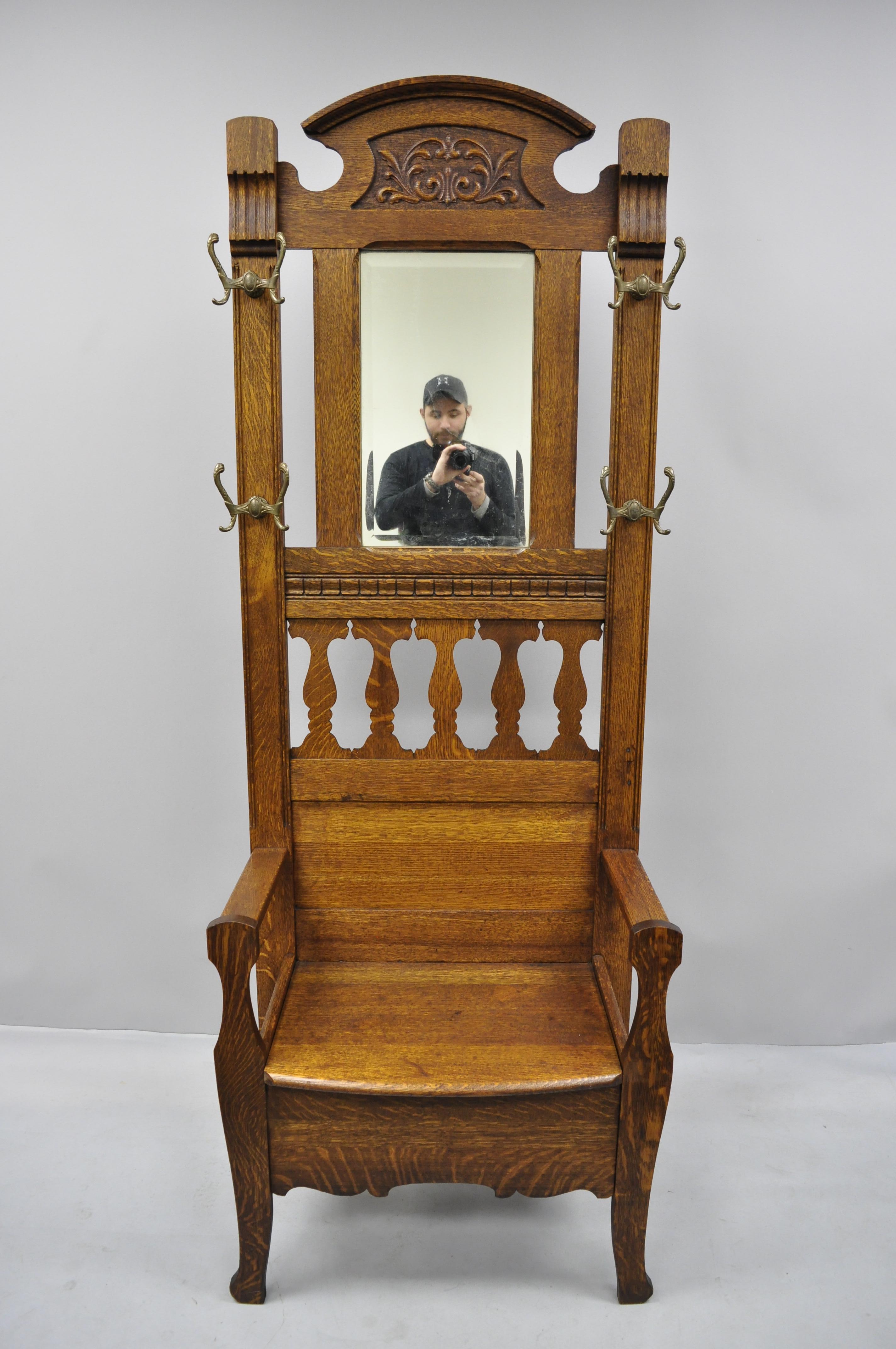 Antique Eastlake Victorian golden tiger oak hall coat tree with storage bench. Item features (4) double coat hooks, beveled glass mirror, solid wood construction, beautiful wood grain and nicely carved details; very nice antique item, circa 1900.
