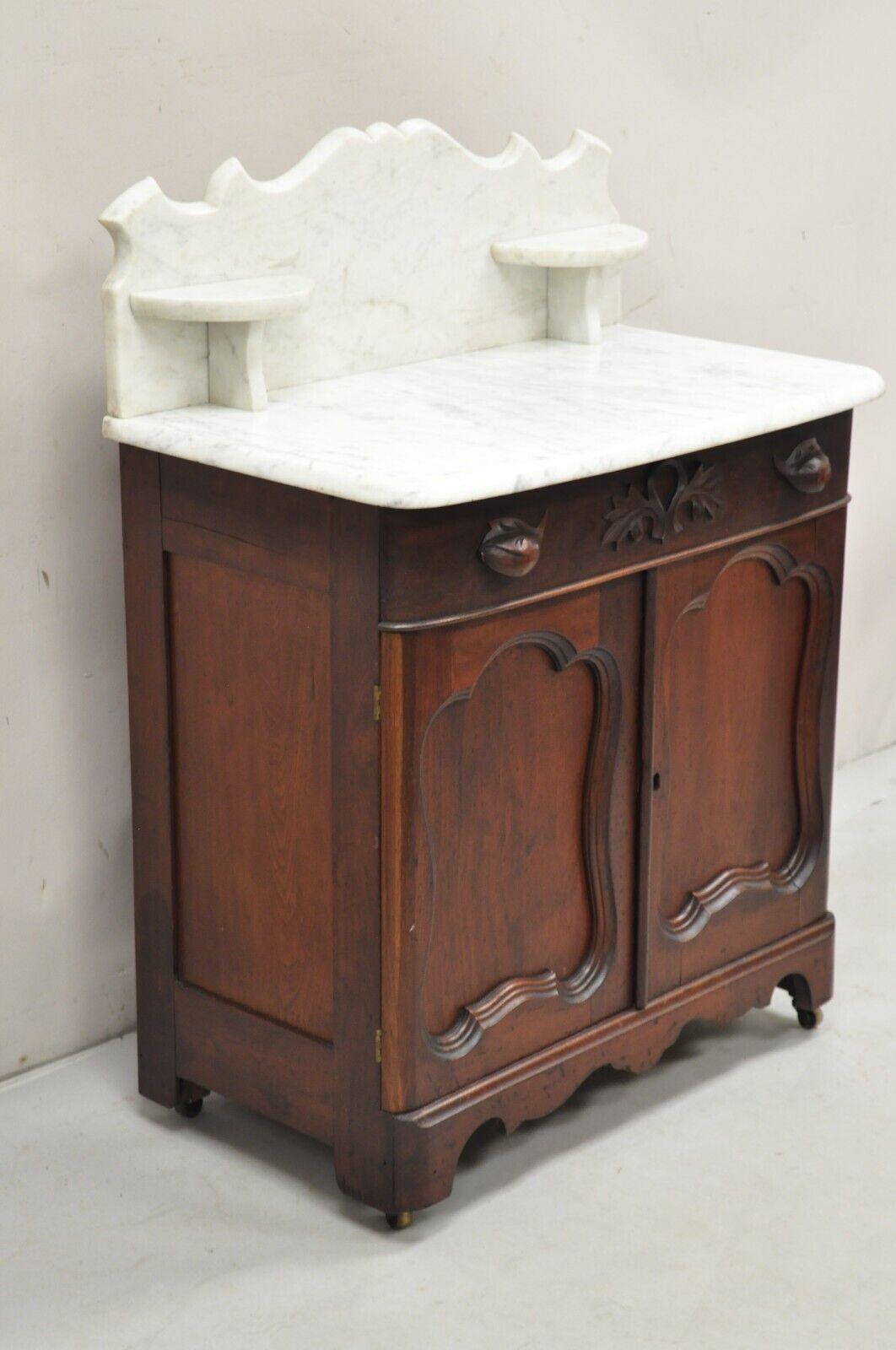 Antique Eastlake Victorian Marble Top Backsplash Walnut Washstand Commode. Item featured carved marble backsplash with 2 small shelves, fruit carved drawer pulls, rolling casters, beautiful wood grain, very nice antique commode, unlocked, no key.
