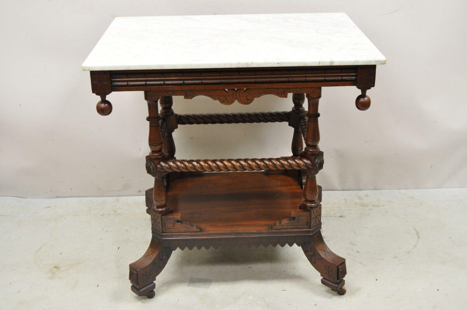 Antique Eastlake Victorian Spiral Carved Walnut Marble Top Two Tier Parlor Table. Item features a white marble top, spiral carved lower tier, rolling casters, ball form finials, very niec antique item. Circa 19th Century. Measurements: 29
