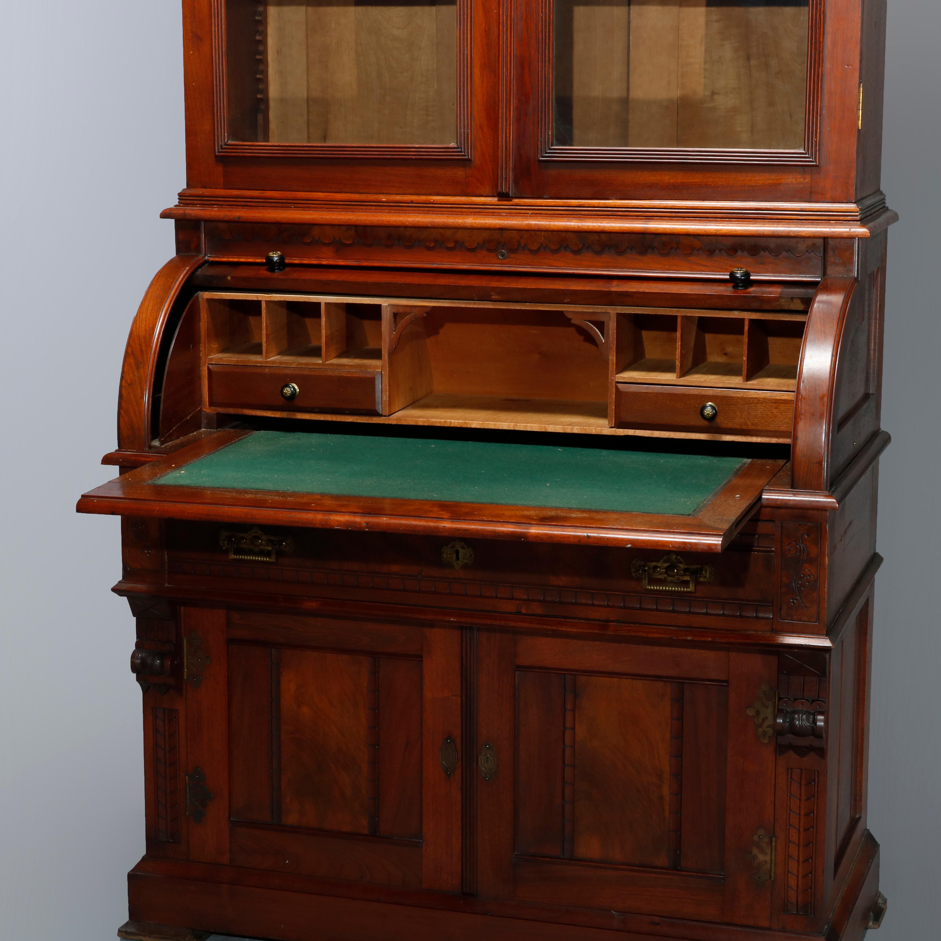 An antique Eastlake secretary offers walnut and burl construction with upper having double glass doors with arched filigree corbels and opening to shelved interior; lower with barrel roll desk with pull-out felted writing surface over a single long