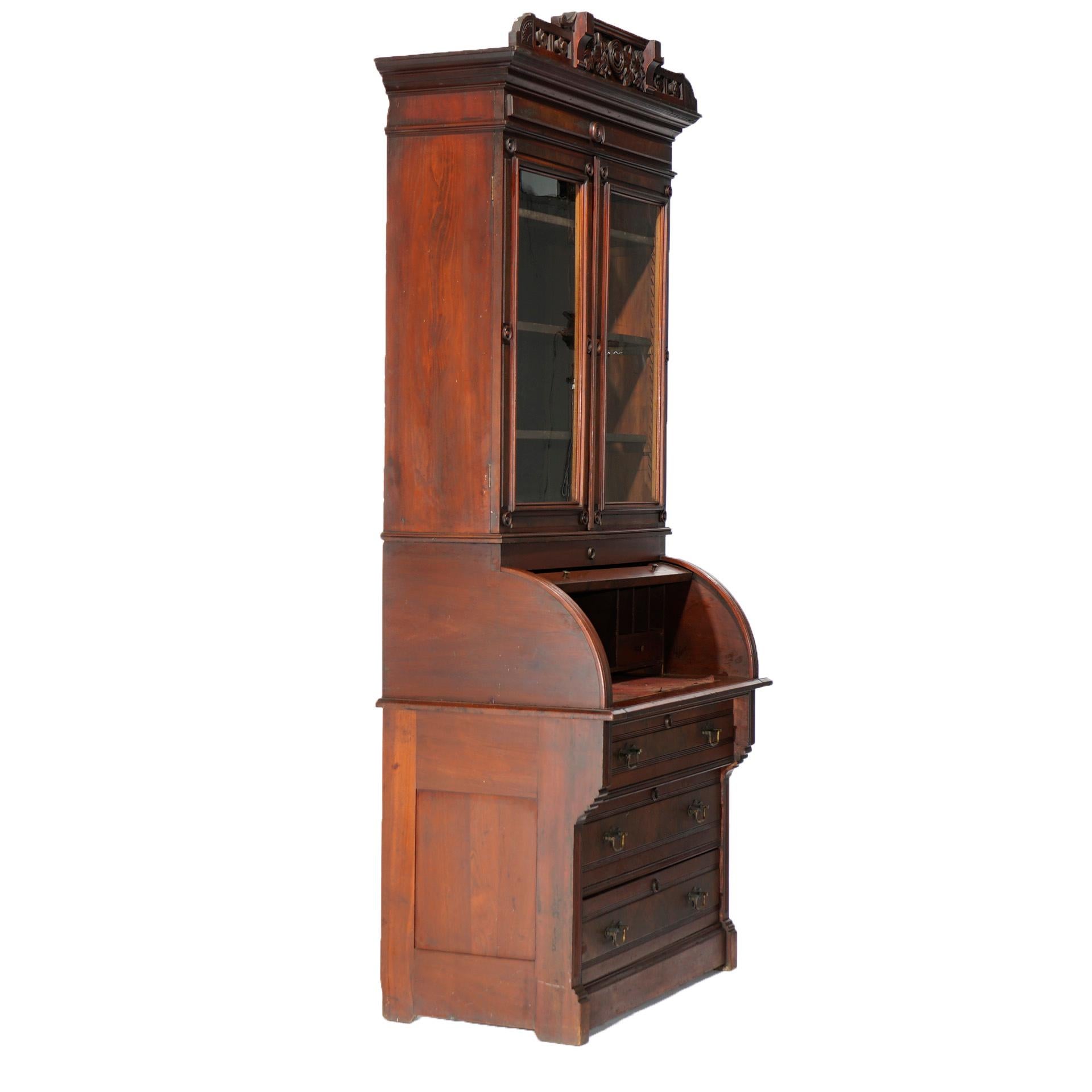 An antique Eastlake secretary offers walnut and burl construction with upper bookcase having carved crest with ivy decorated crest over double door case with adjustable shelf interior surmounting lower case with barrel roll desk opening to interior