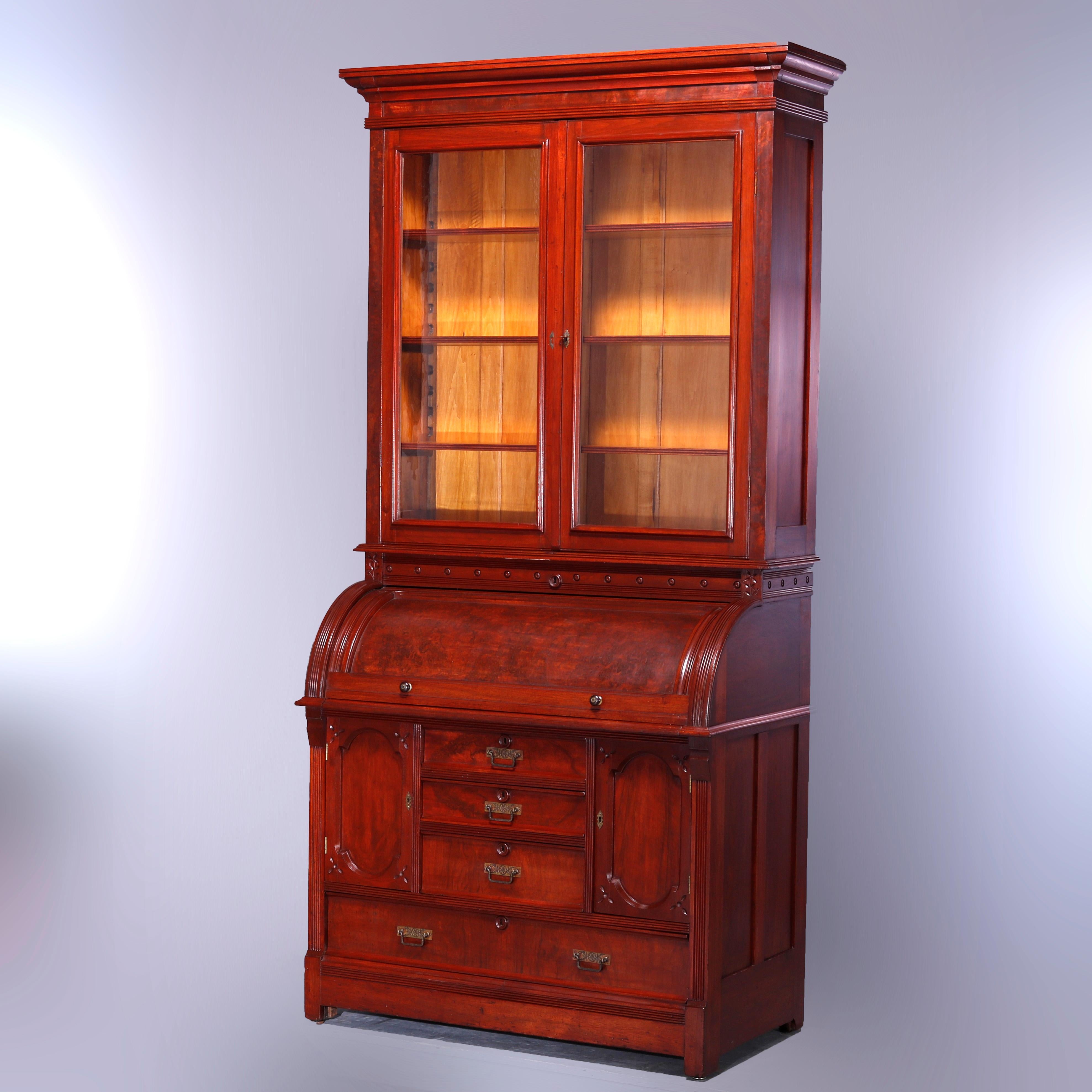 Antique roll top secretary offers walnut and burl paneled construction with upper bookcase with double glass doors opening to shelved interior and surmounting cylinder desk having central drawer tower with flanking cabinets and lower long drawer,