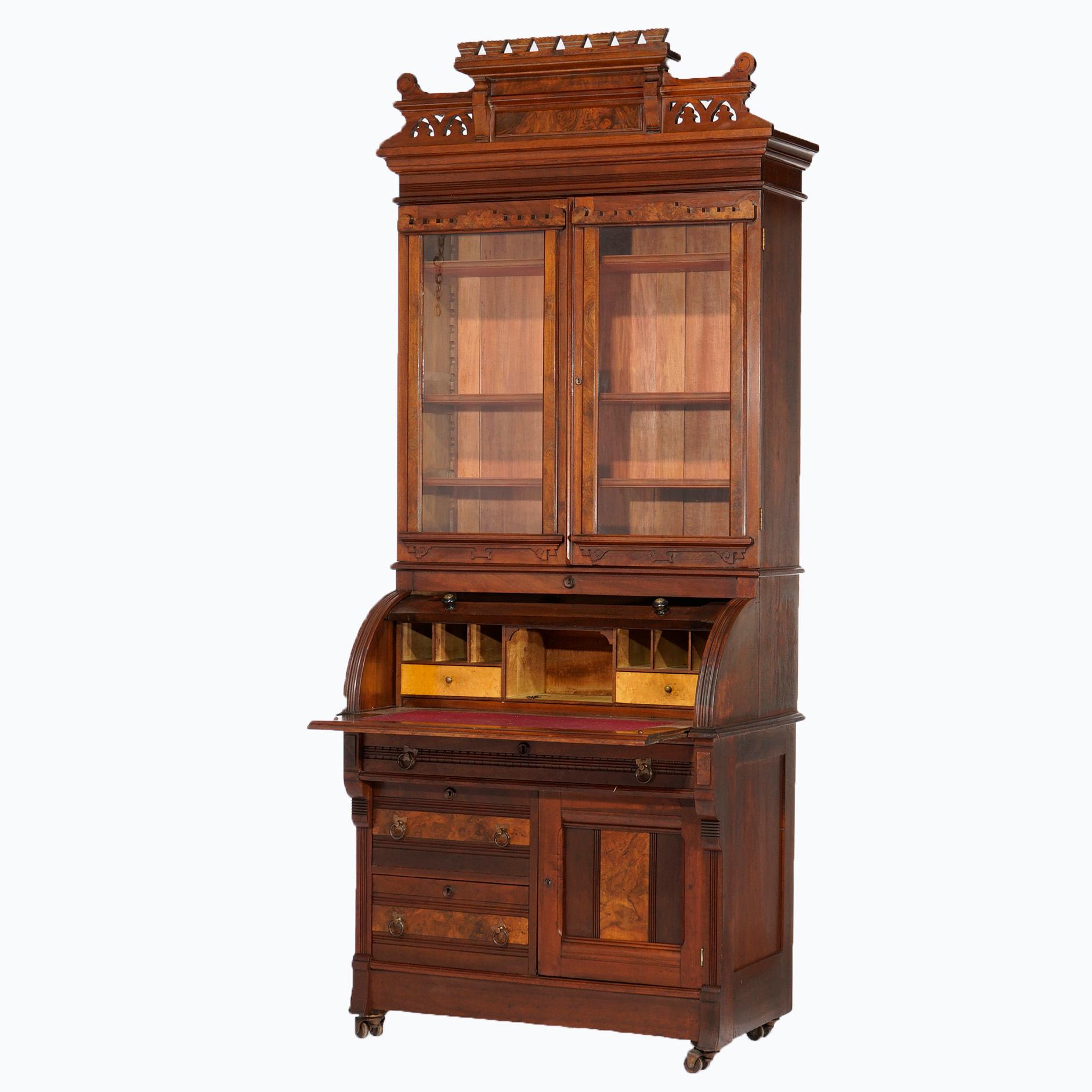 An antique Eastlake secretary offers walnut and burl construction with pierced crest over double glass door bookcase with double glass doors opening to shelved interior over lower with barrel roll desk over drawers and lower cabinet,
