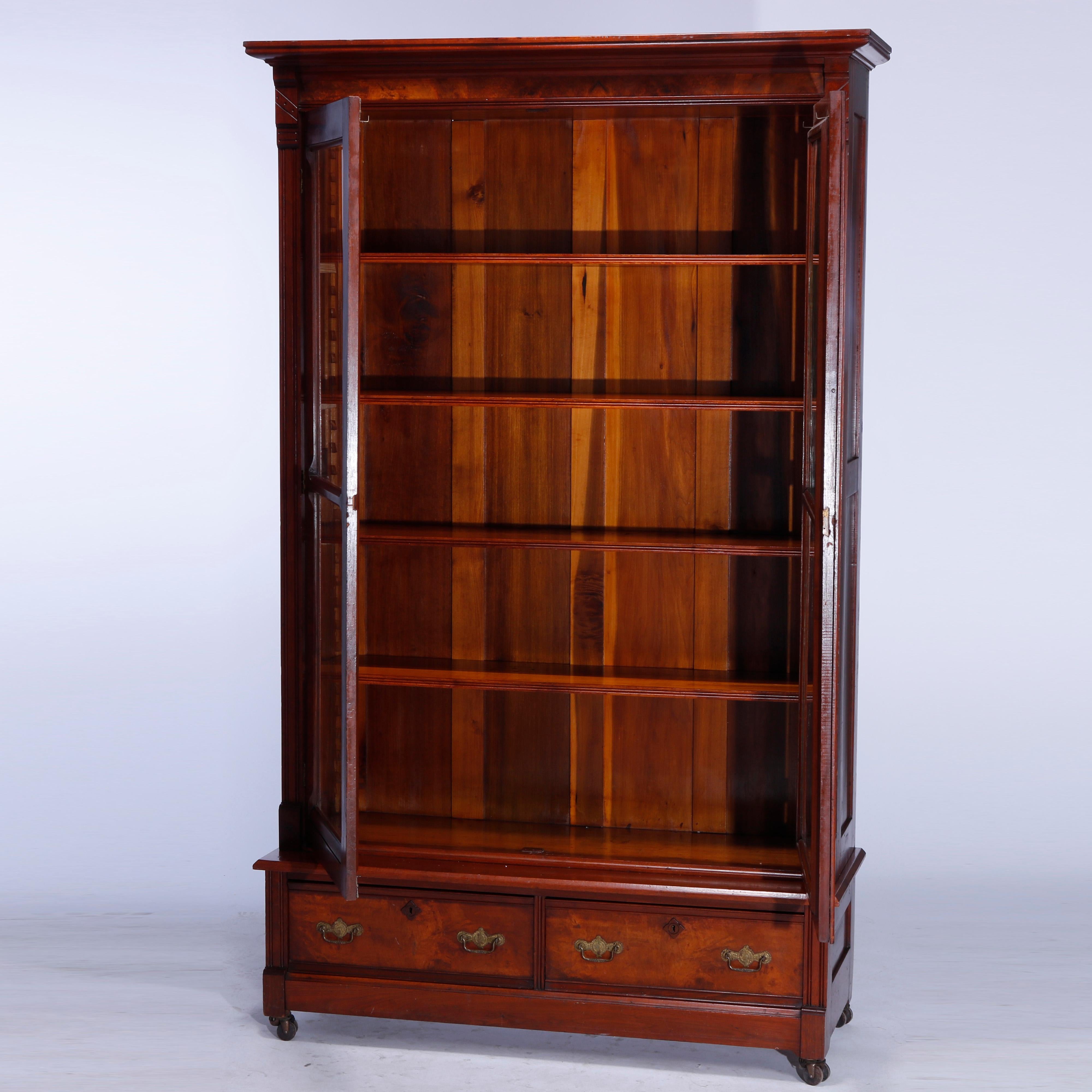 An antique Eastlake bookcase offers walnut and burl construction with double glass doors opening to adjustable shelf interior over two lower storage drawers, raised on straight legs with casters, incised decoration throughout, c1890

Measures -
