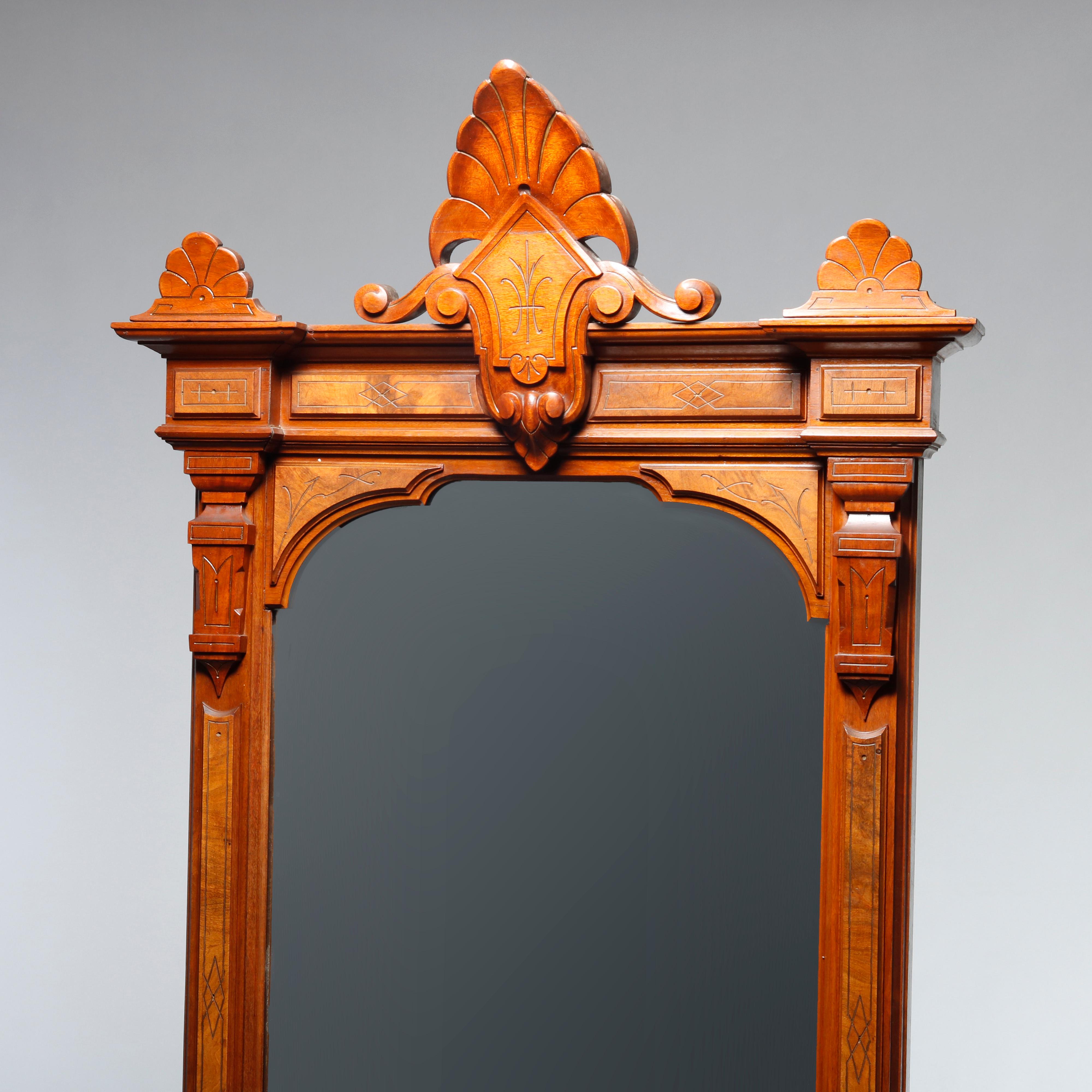 An antique Eastlake pier mirror offers walnut construction with carved stylized shell and shield crest with flanking scroll elements and surmounting burl paneled frame with incised decoration, seated on base with shaped marble top,