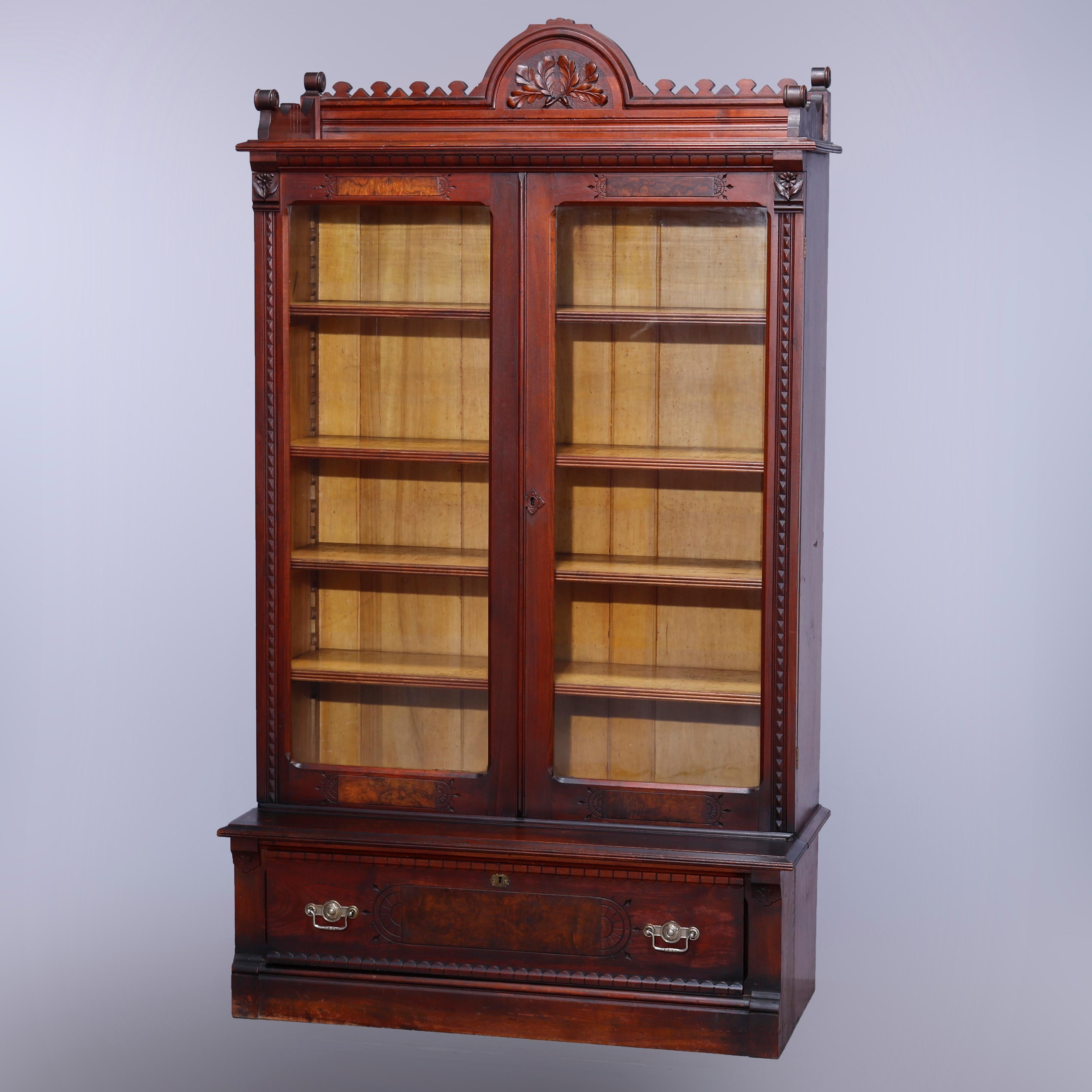 An antique Eastlake enclosed bookcase offers walnut construction with burl insets having upper gallery with central demilune crest having carved foliate elements and flanking cutout rail surmounting case with double glass doors opening to adjustable