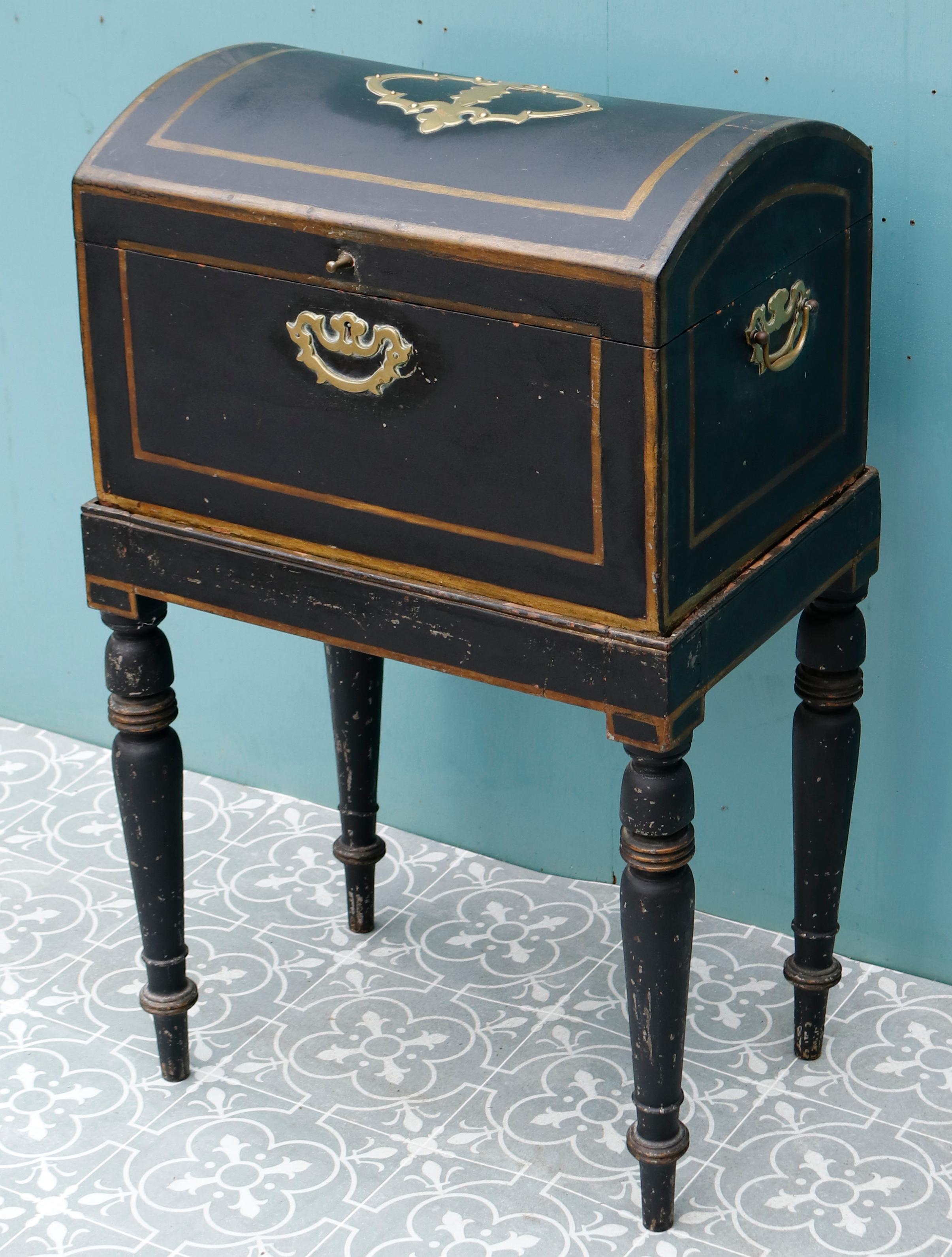 A painted domed box on stand with central brass cartouche to the lid, brass handles to each side, the stand with bun topped tampering cylindrical legs and spindle feet.