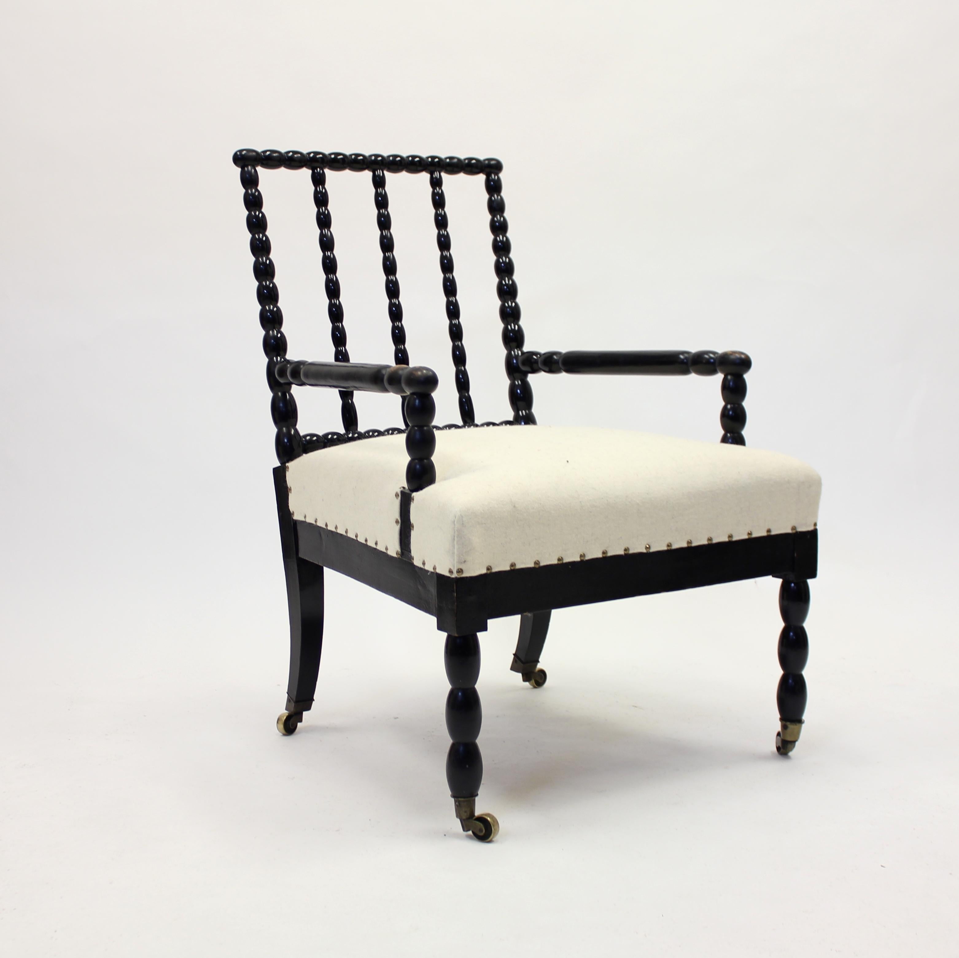 Antique ebonized bobbin turned chair, from later part ot the 19th century or early part of the 20th century, on brass castors with new off white felt upholstery. The back cushion is removable. Most likely British. Very good vintage condition with