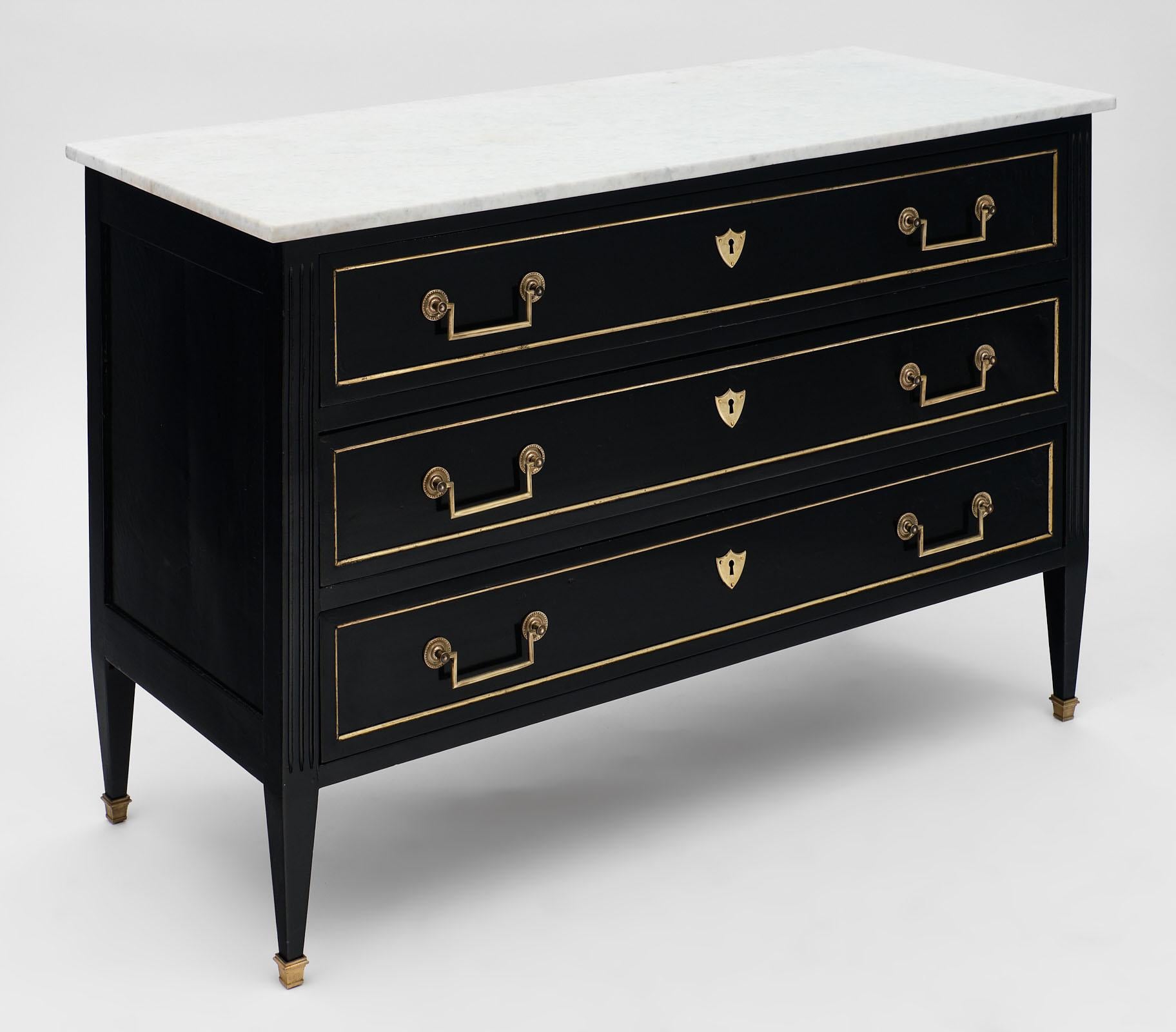 Louis XVI style antique ebonized chest with three dovetailed drawers, gilt brass hardware and trim, and lovely tapered legs. This commode chest features a beautiful Carrara marble slab top and an ebonized finish with French polish for a museum