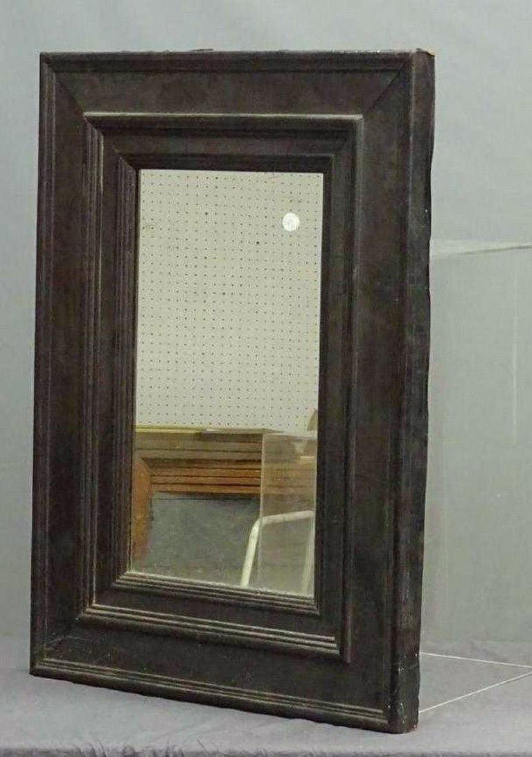 The antique Regency inspired wall mirror has a wide ebony metal frame resembling architectural molding layered onto a wood base. This mirror has a modernist feel and neoclassical at the same time. The wood back has a brass chain secured for hanging.