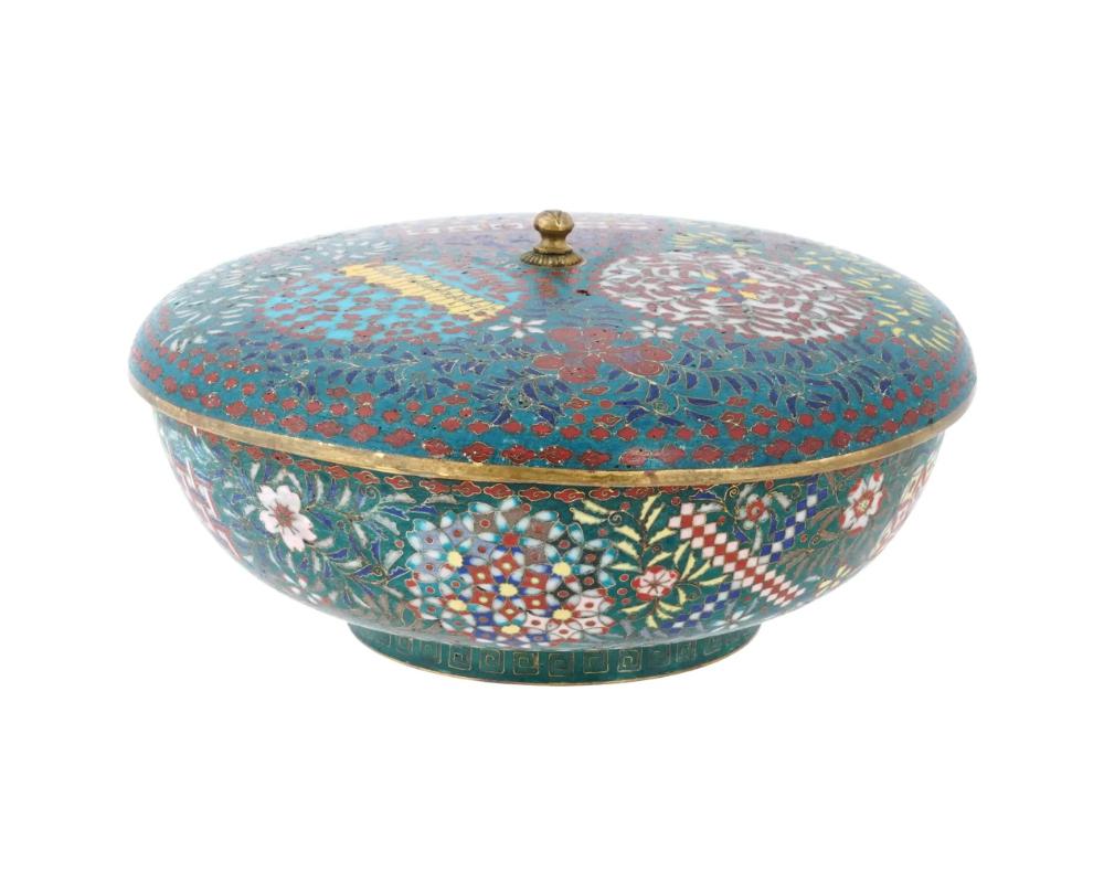 An antique Japanese brass enamel ceremonial food container with a cover adorned with a pointed finial. Characterized by cloisonne floral designs adorning the surface, this ceremonial container showcases the meticulous artistry typical of Japanese