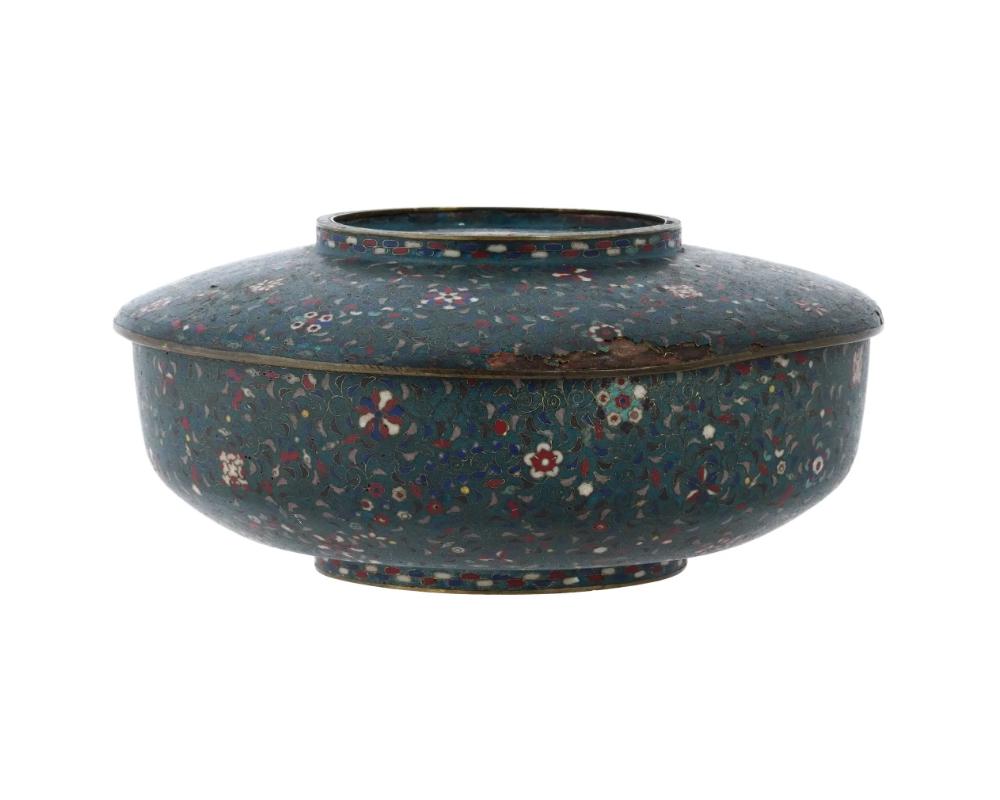 An antique Japanese flat brass enamel ceremonial food container with a cover. Characterized by cloisonne floral designs adorning the surface, this ceremonial container showcases the meticulous artistry typical of Japanese decorative arts during the