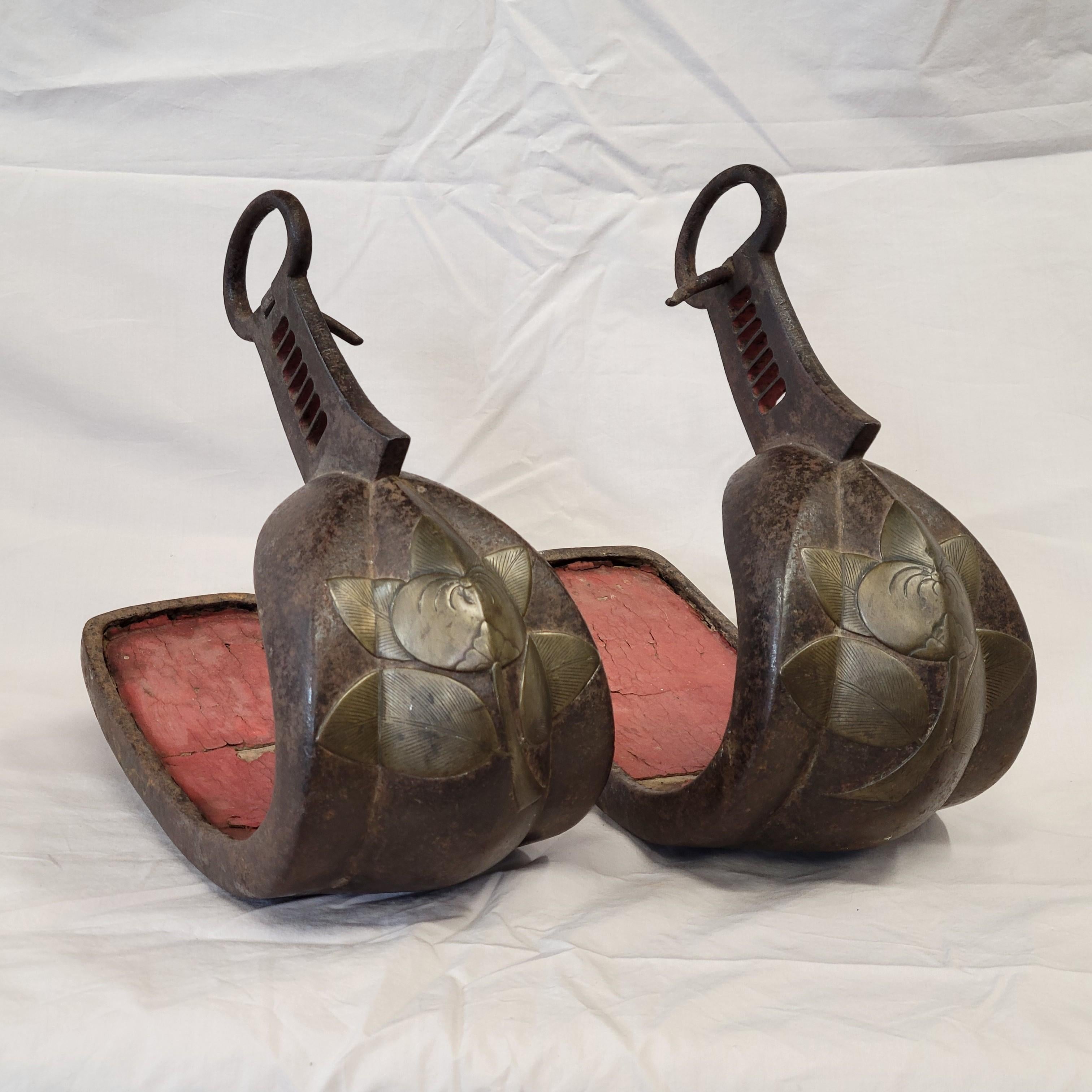 A pair of antique Edo period (1603–1867) Japanese Samurai Abumis (stirrups for horseback-riding) expertly crafted out of cast iron with brass or bronze inlay in the form of a stylized flower or fruit  The interior of the stirrup, where the rider