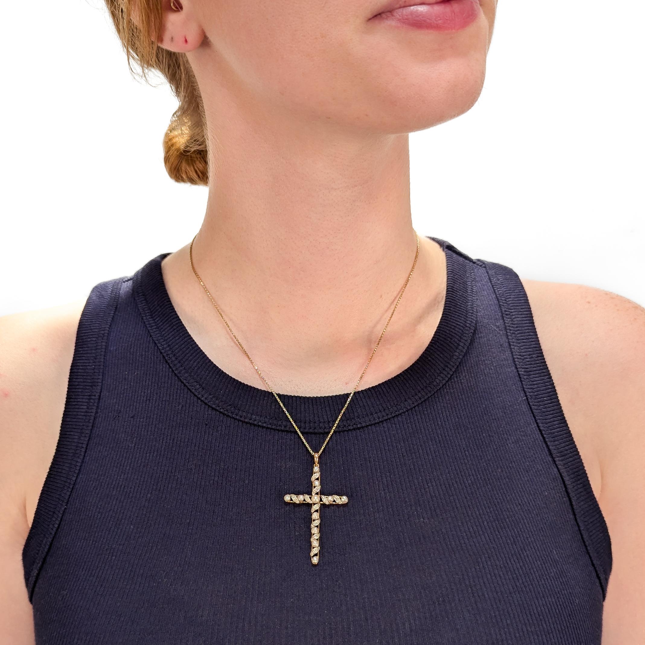 Croix pendante en or ancien, diamants et perles pour un collier.

En or jaune 14 carats.

En forme de croix centrée sur une perle blanche ronde.

Les extensions de la croix sont serties d'un motif alterné de diamants pavés dans des volutes d'or