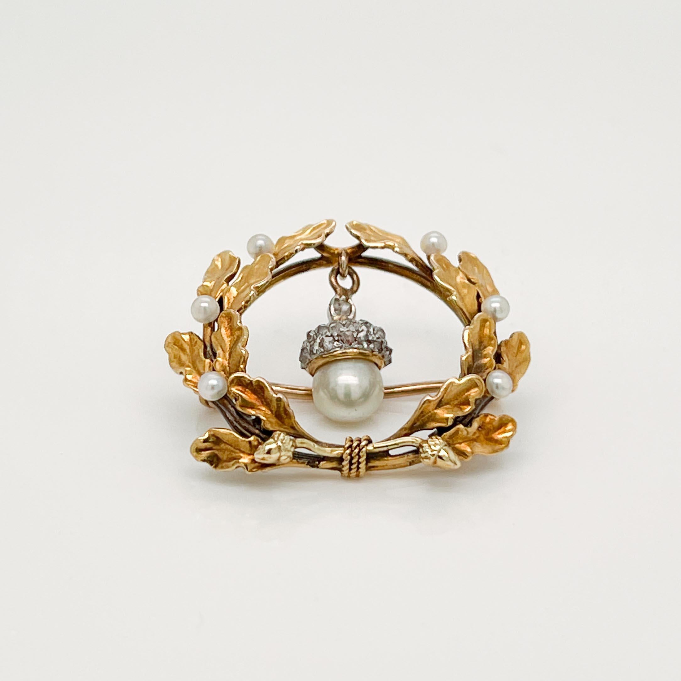 A fine signed antique Edwardian brooch by Krementz. 

In 14k gold. 

In the form of a wreath of oak leaves offset by seed pearls. The wreath supports a figural acorn drop comprised of a pearl bottom & a diamond encrusted top. Small cords with acorn