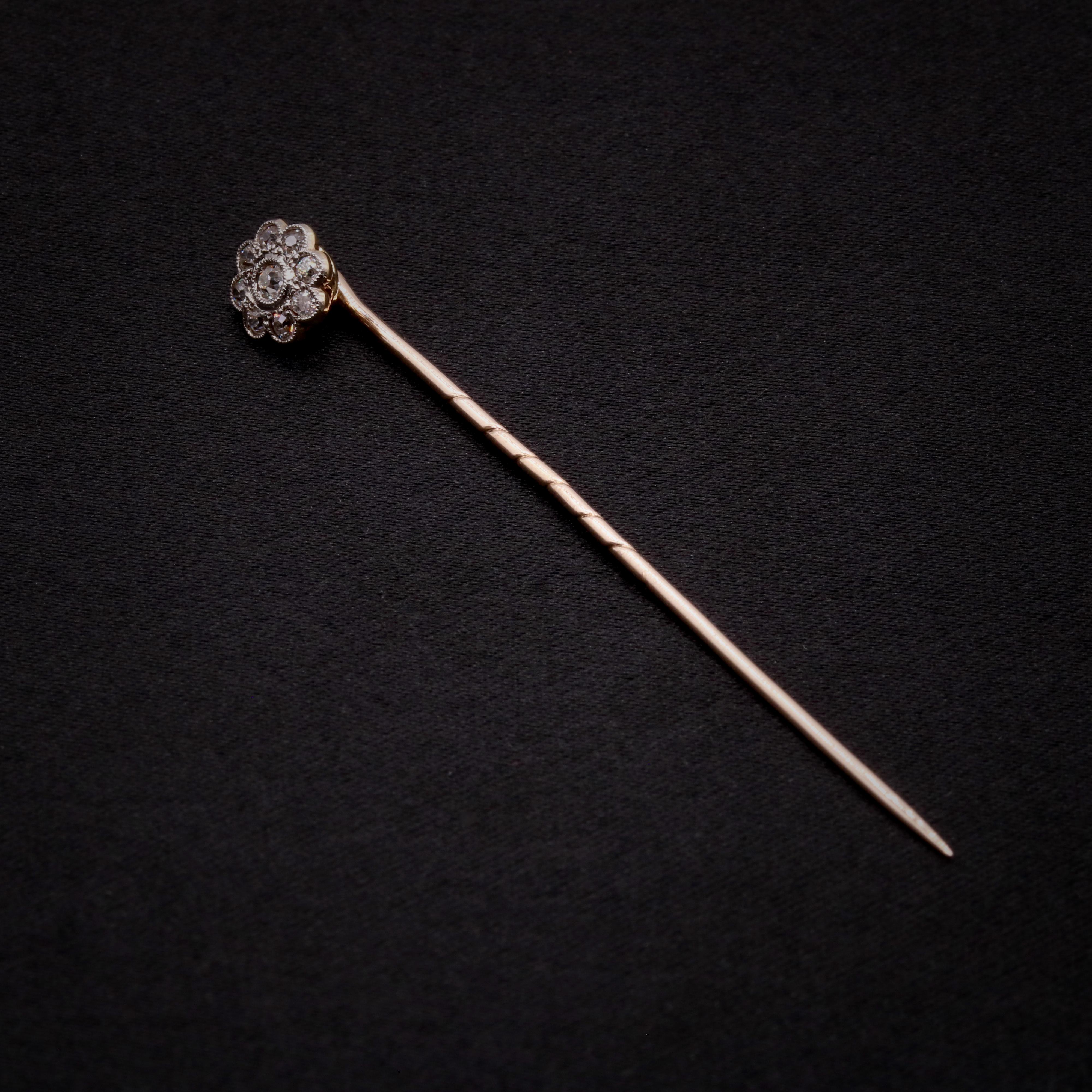 An Edwardian diamond, platinum and yellow gold stick pin, comprising one old European cut diamond, and eight old single cut diamonds, set in platinum and 15 karat yellow gold, with a 9 karat yellow gold pin. 

This pretty stick pin is designed as a