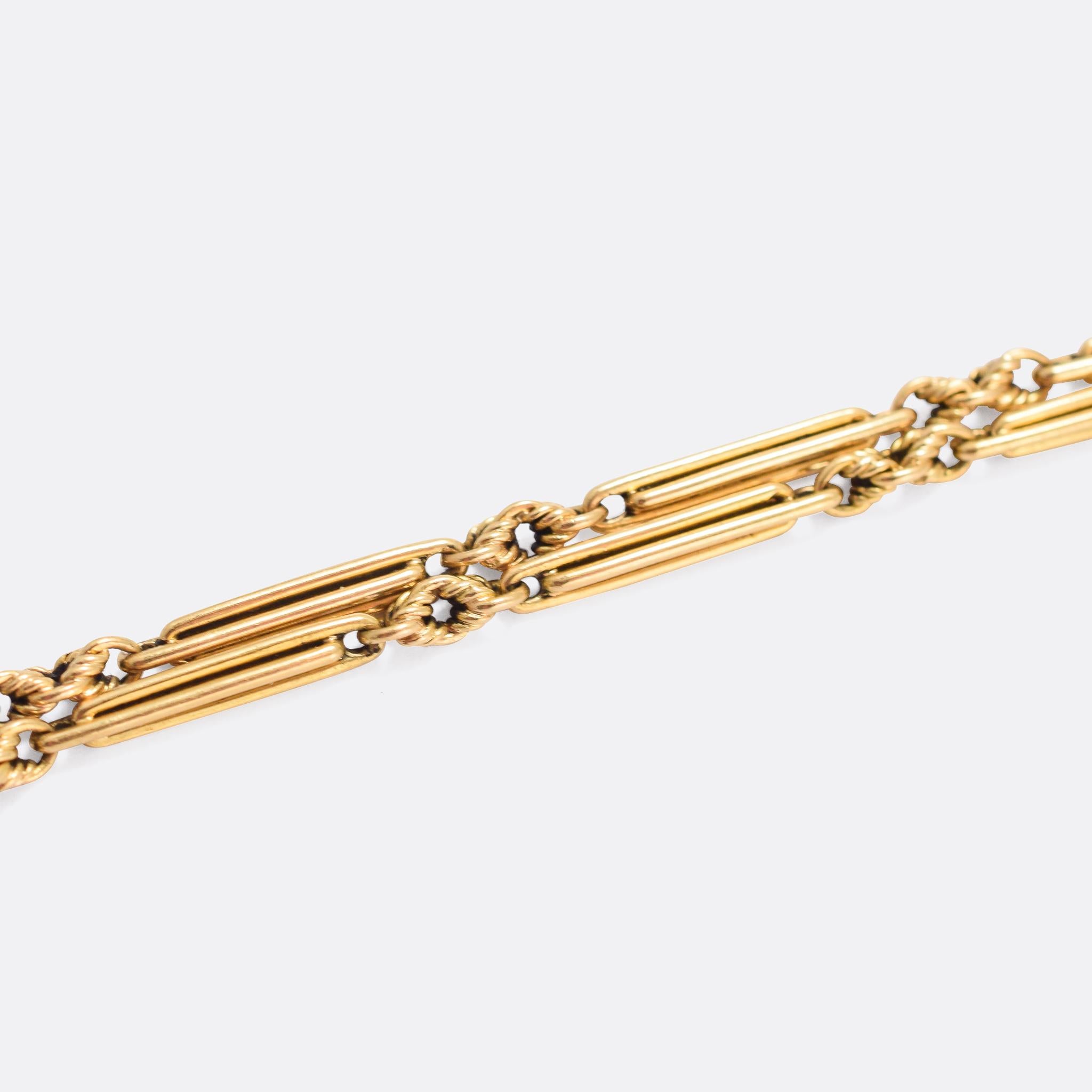 Antique 18k gold trombone link chain, circa 1910. Of heavy construction, the long trombone links are separated by infinity knot joiners; it fastens with a dog tag clasp at one end, and a ring bolt at the other. Originally intended as a pocket watch