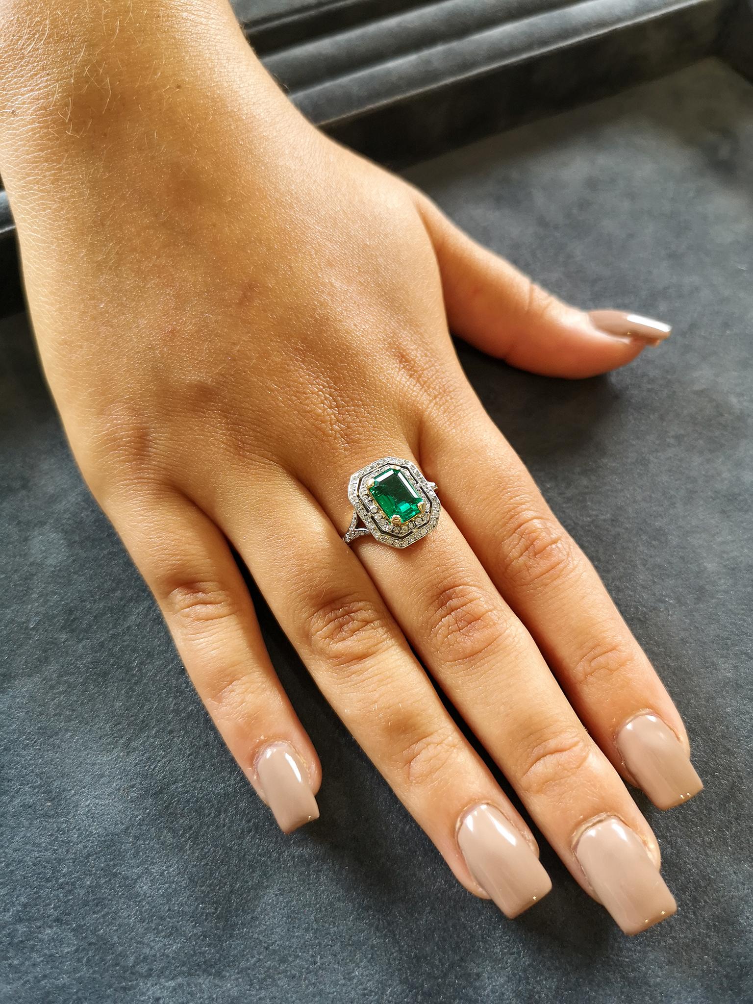 An exceptional antique cluster ring, circa 1905. The central emerald-cut emerald of astonishing colour and clarity, mounted in four 18-carat gold claws. Surrounded by a double row of bead-set old-cut diamonds. Bifurcated diamond set shoulders, lead