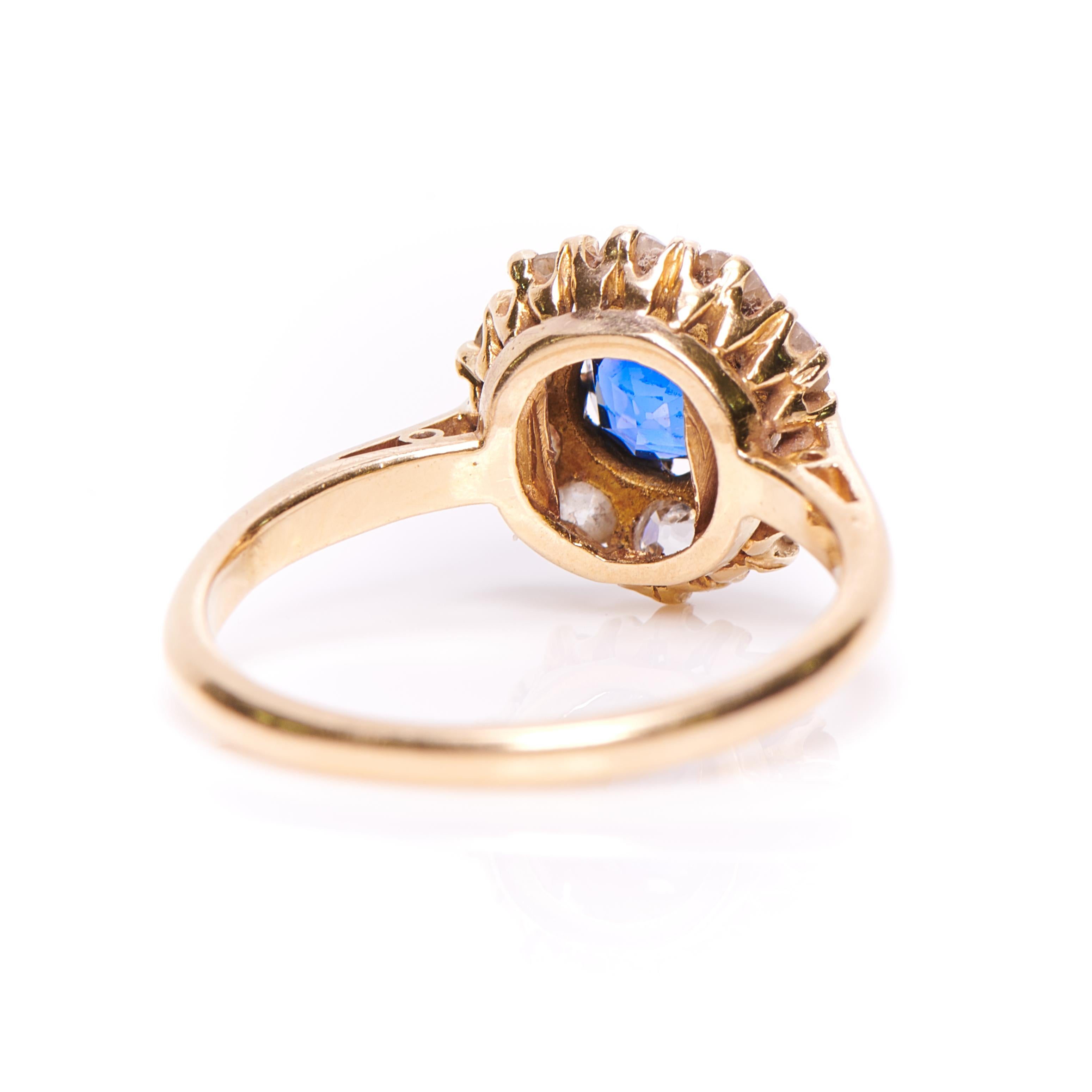 A beautifully simple sapphire and diamond cluster ring, circa 1900. A vibrant blue sapphire sits in the centre, encircled by a single row of old cut diamonds in a typical late Victorian/early Edwardian coronet setting crafted in yellow gold. The