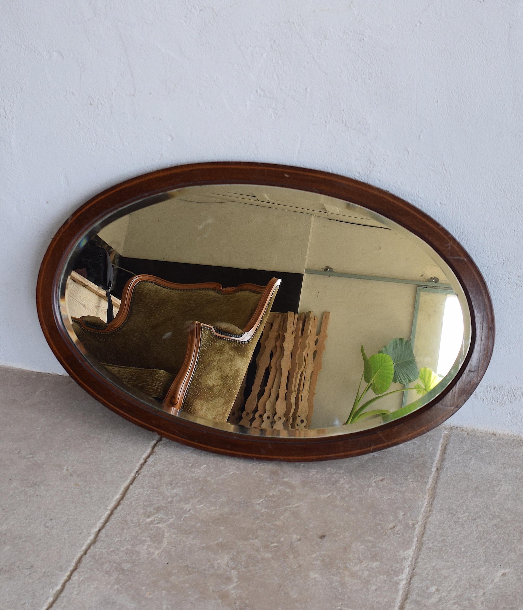 An elegant antique Edwardian (1901-1910) oval mirror made of mahogany which has a warm patina across its surface. The richly figured mahogany frame has a simple design inlay with a chequer banding around the edges. It is a decorative object with