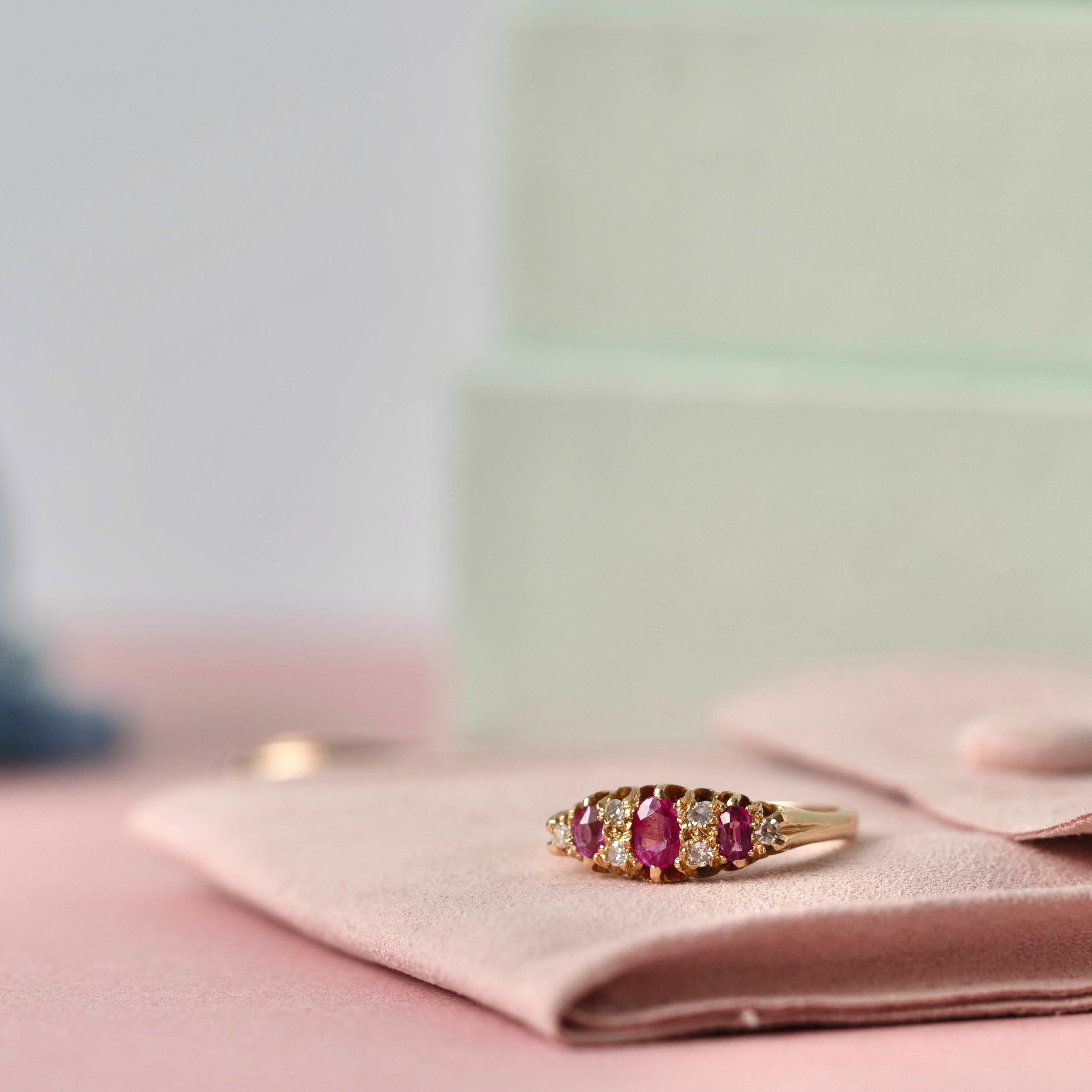 This stunning piece of jewelry is an authentic representation of Edwardian elegance, crafted in 1906. The ring features a trio of vivid oval rubies, interspersed with sparkling diamonds, creating a harmonious balance of color and brilliance. Set in