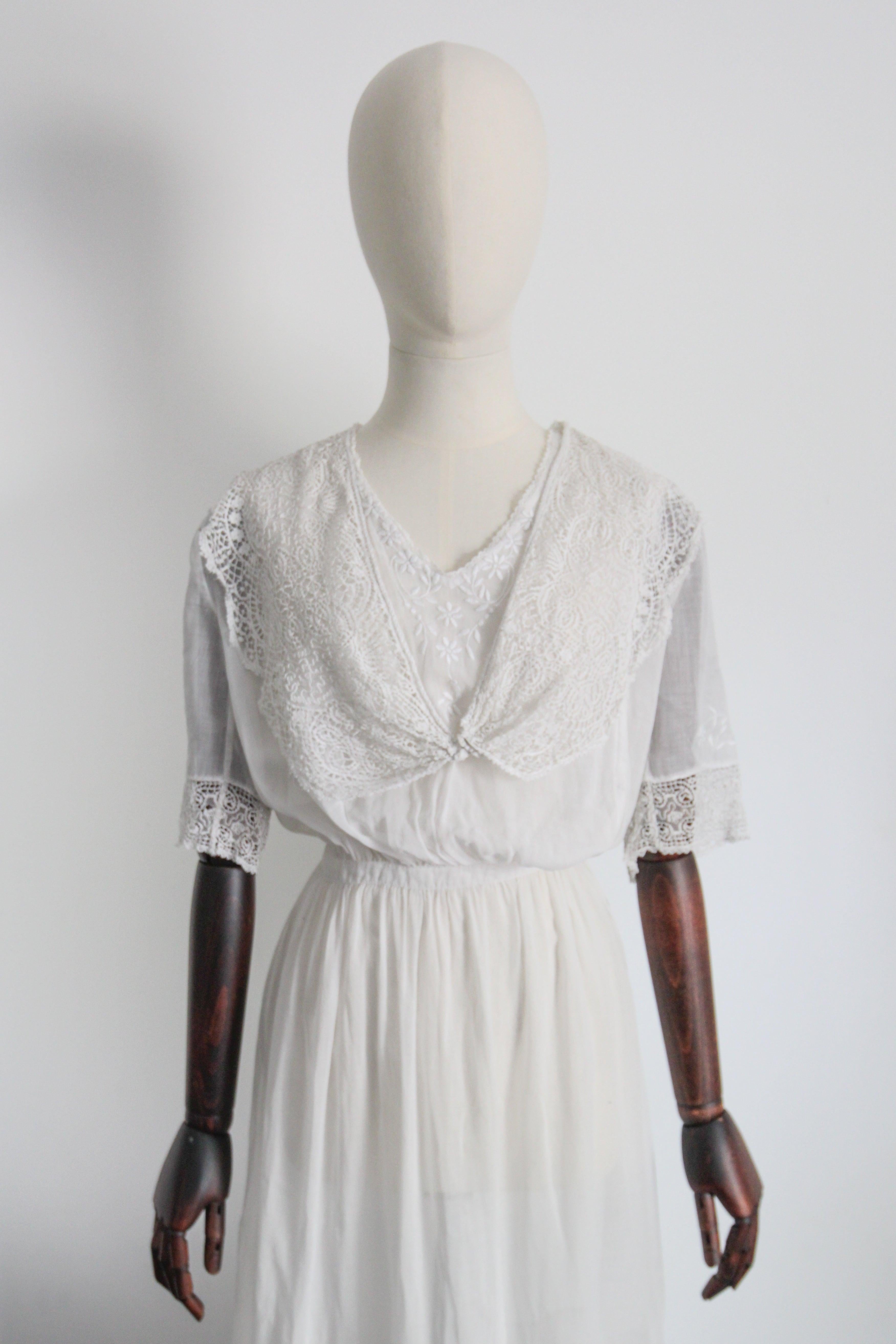 This magnificent 1910's Edwardian lawn cotton dress, with detailed embroidery and lace accents is a rare piece to behold.  

The rounded neckline of the dress, is framed by a delicate lace border which sets off the trailing floral embroidery along