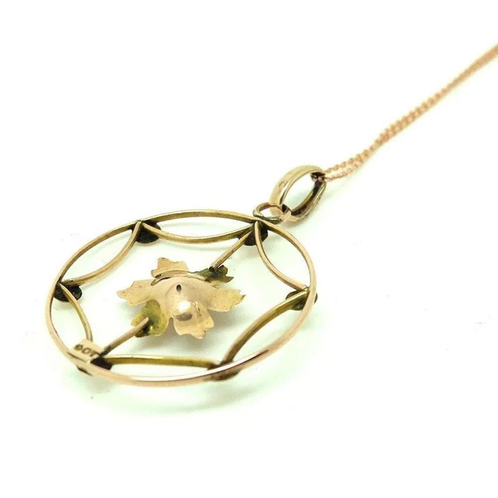 Élégant et intemporel, ce pendentif antique Elegne est un bel exemple du design du début du XXe siècle. Réalisé en or rose 9ct, le pendentif présente un délicat motif floral ajouré autour d'une perle lumineuse. Le design est rehaussé par des détails
