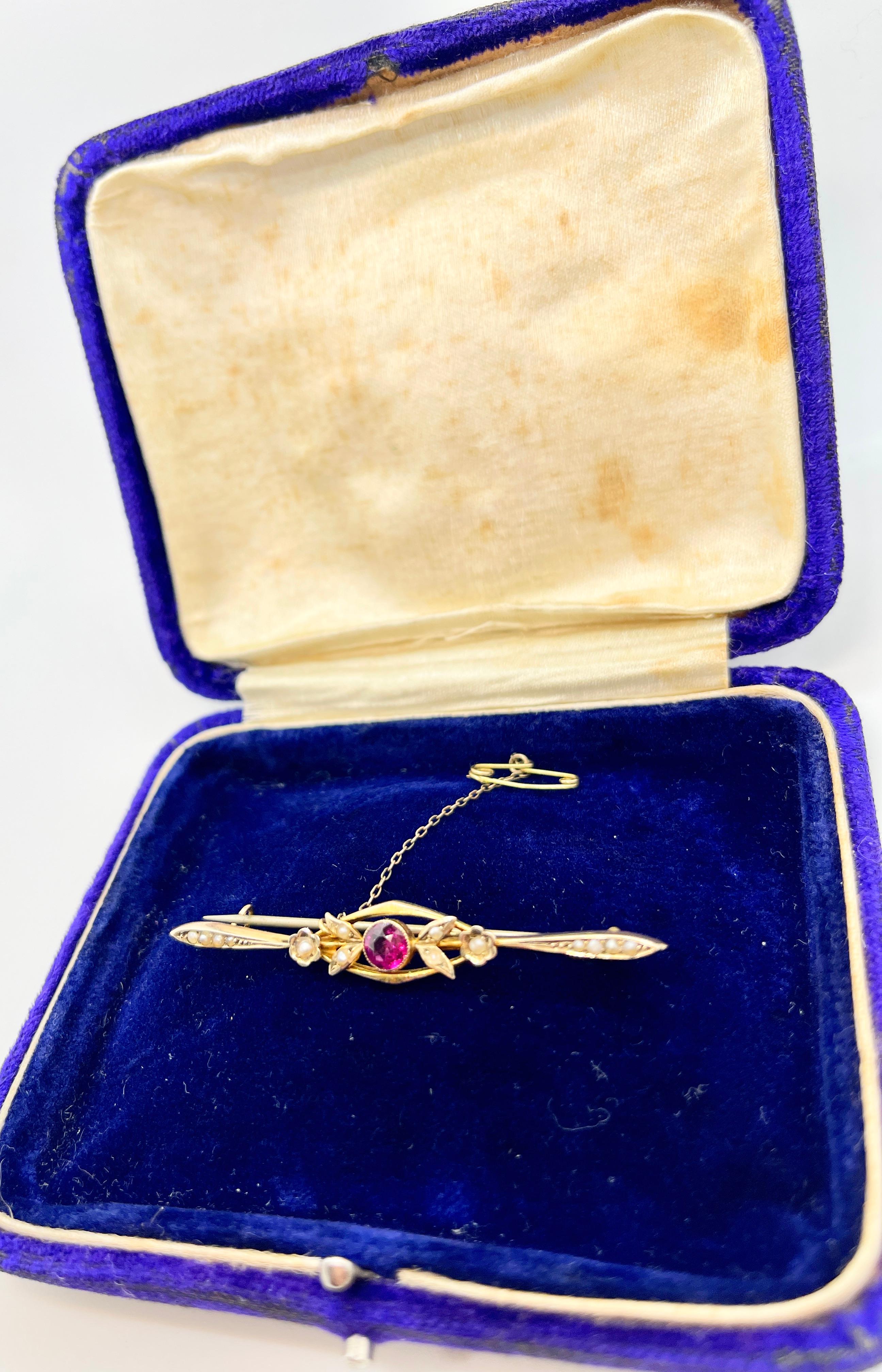 This antique piece features a natural, round Ruby centring 14 seed pearls of graduating size. The bar style brooch is crafted in 9ct yellow gold (stamped) with floral and leaf motifs that are typical of this era, Circa 1910. 

The brooch bears the