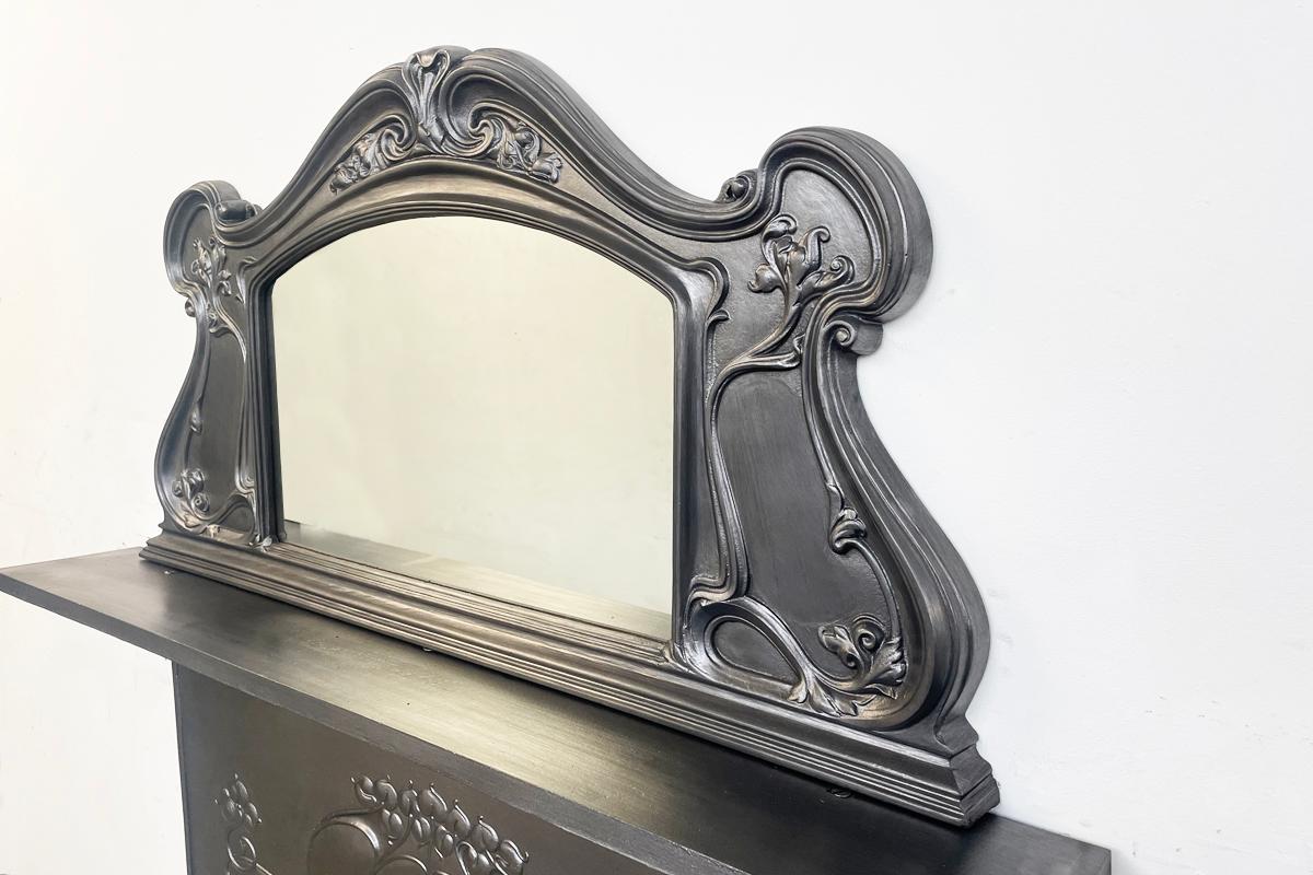An antique Edwardian cast iron overmantle mirror in the Art Nouveau manner.

Finished with traditional black grate polish with a replacement mirror plate.

Overall 111 cm wide at the base by 59cm high
