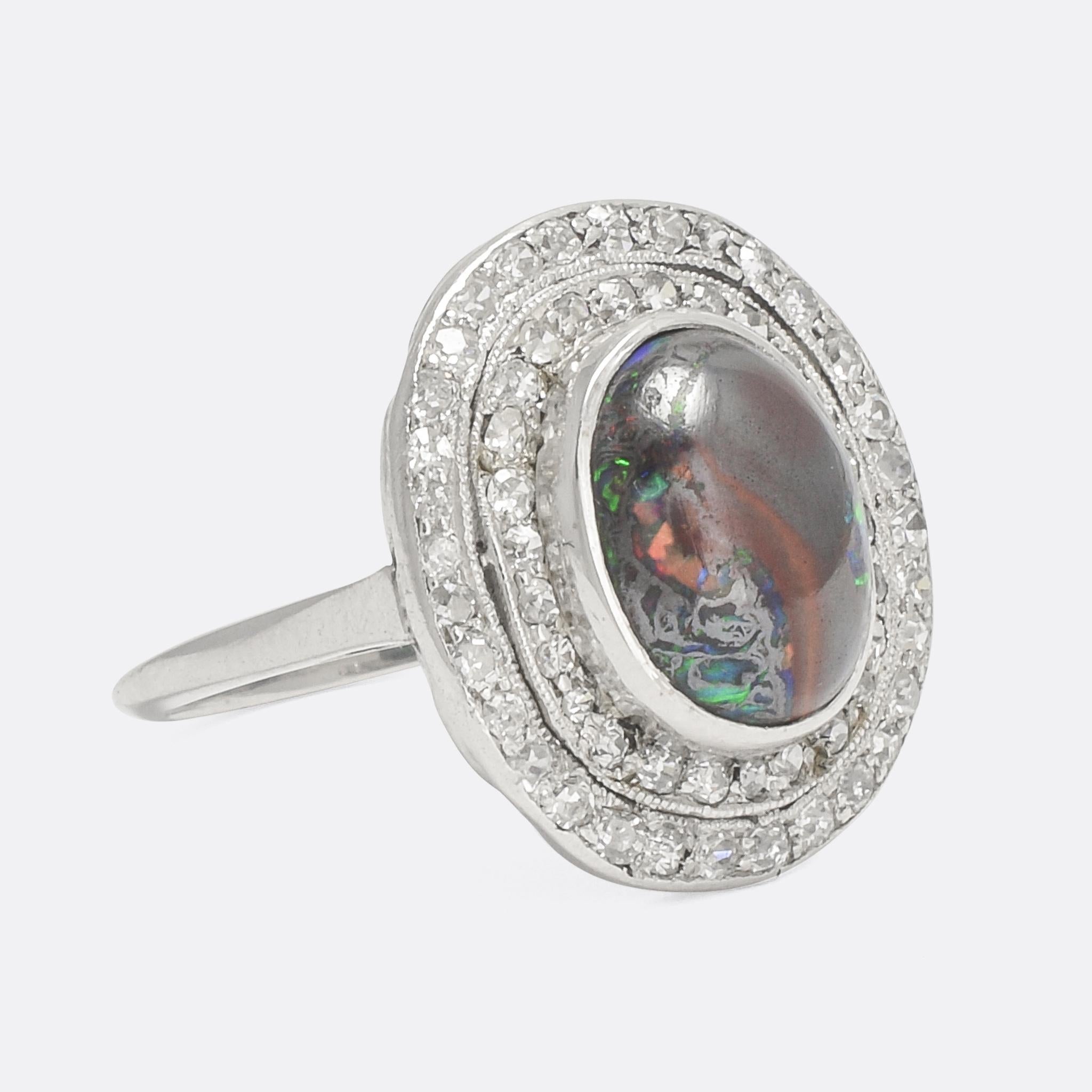 A spectacular Edwardian double halo ring set with a lively black opal in the centre. The stone displays vivid flashes of red, blue, green and orange, with a subtle red streak down the middle. Modelled in platinum throughout with an openworked