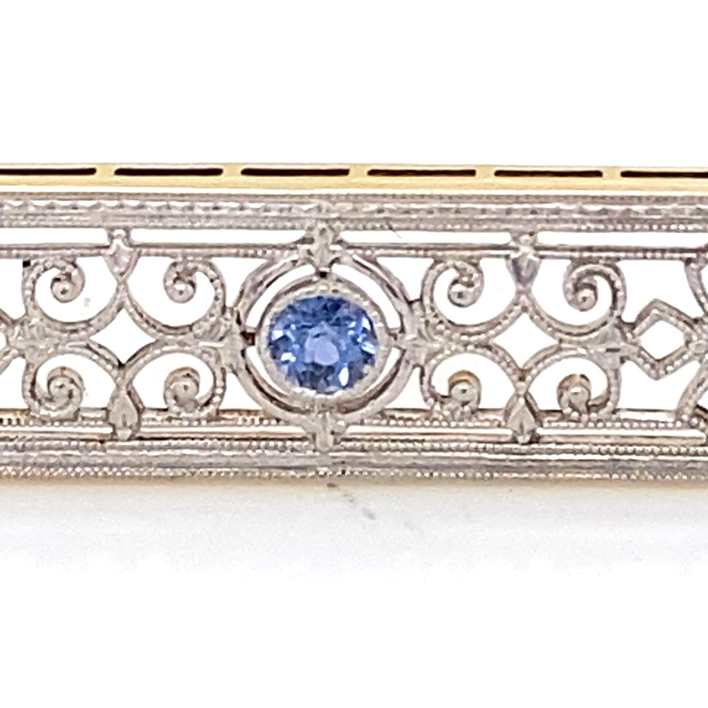 This Edwardian platinum and 14 karat yellow gold brooch features an approximately 0.13 carat round pastel blue faceted sapphire that is bezel set in a platinum.  Measuring approximately 1 5/8