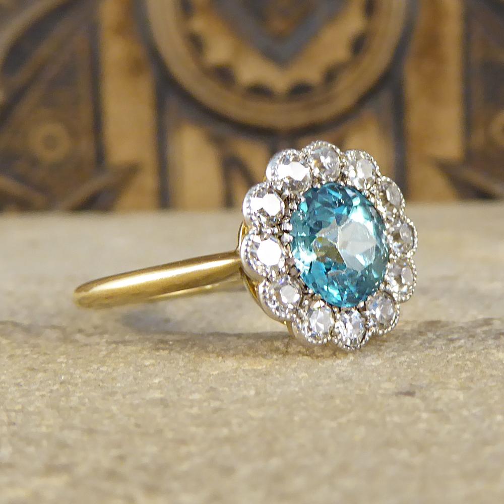 This stunning antique ring has been hand crafted in 18ct Yellow Gold in the Edwardian era, highlighting the delicate style of this time. Featuring a single beautiful blue Zircon weighing 1.00ct inside a cluster of 12 European cut Diamonds weighing