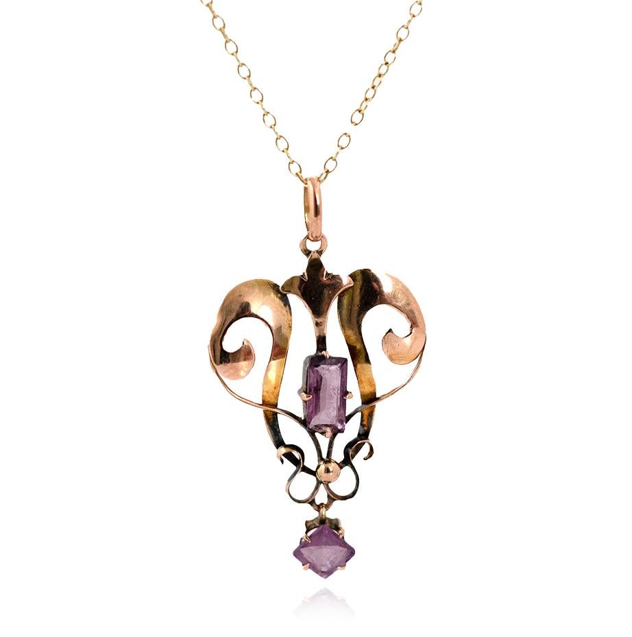 This striking pendant captures the elegance of the Edwardian era, crafted in soft 9ct rose gold with sweeping openwork scrolls and delicate proportions. At its centre rests a rectangular-cut amethyst, glowing with purple vibrancy, while a suspended