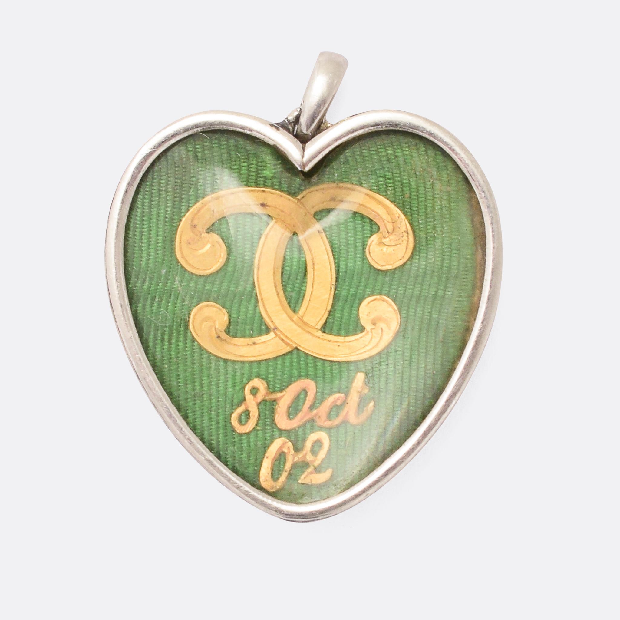An exceptional antique heart pendant by Cartier Paris. One side features a diamond-set crossed torches motif on a vibrant green guilloché enameled backdrop. Turning it over we find the initials CC - in high carat yellow gold - and a date: October